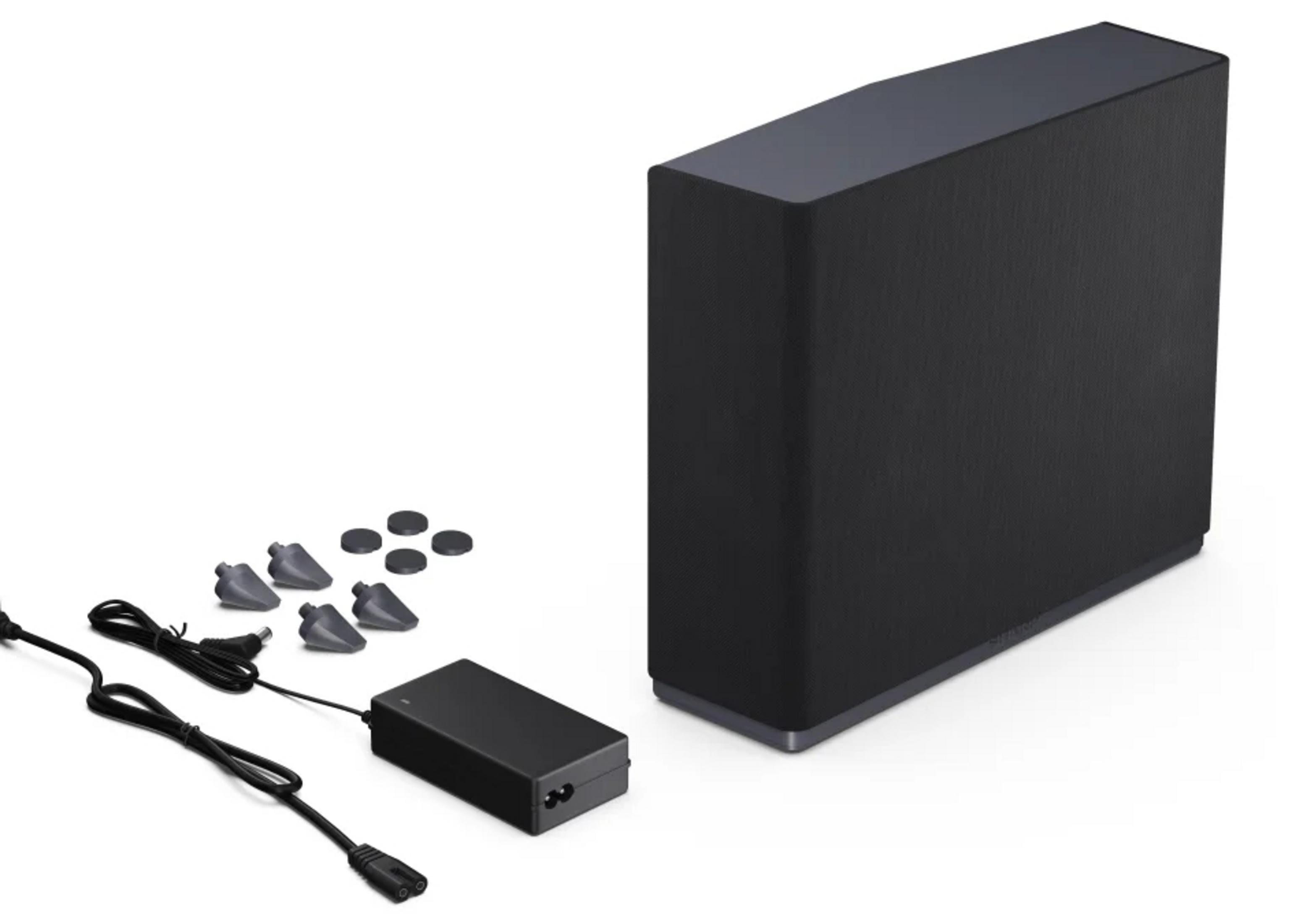 Altavoz negro con adaptador de corriente y pies sobre fondo blanco.