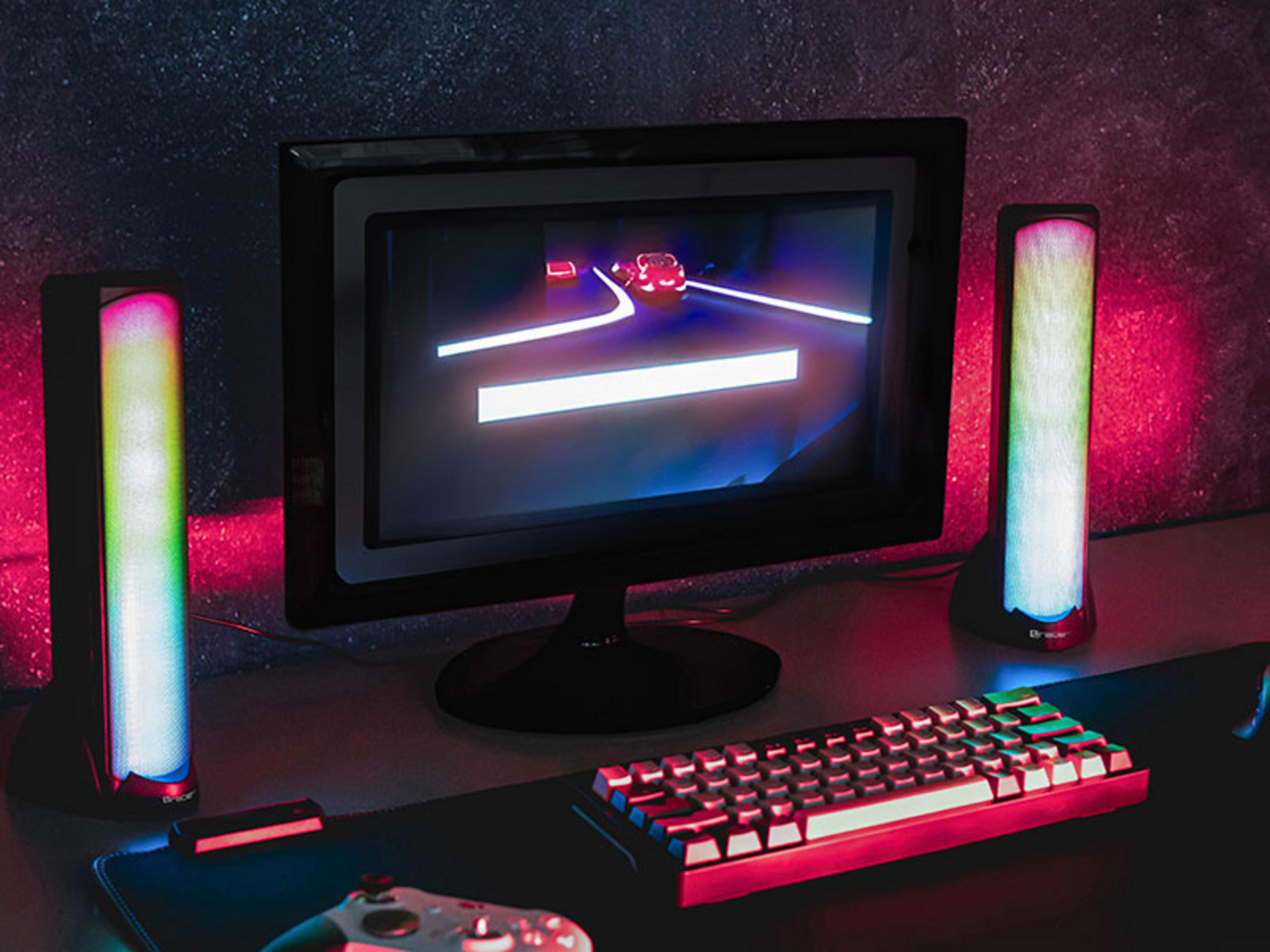 Configurazione da gioco con monitor, tastiera, controller e luci in una stanza buia.
