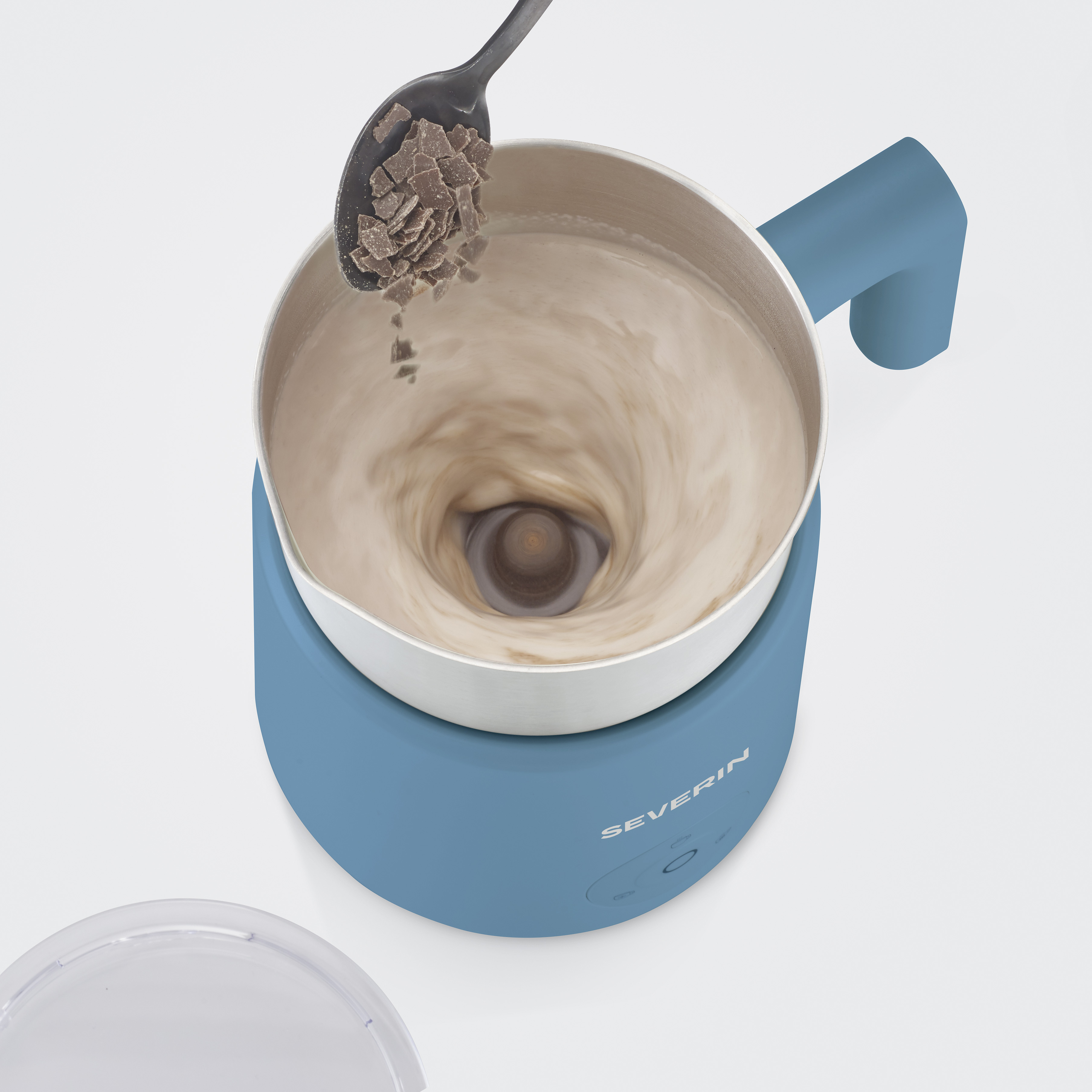 Schokoladenstückchen fallen von einem Löffel in ein wirbelndes, cremiges Getränk in einer blauen Maschine.