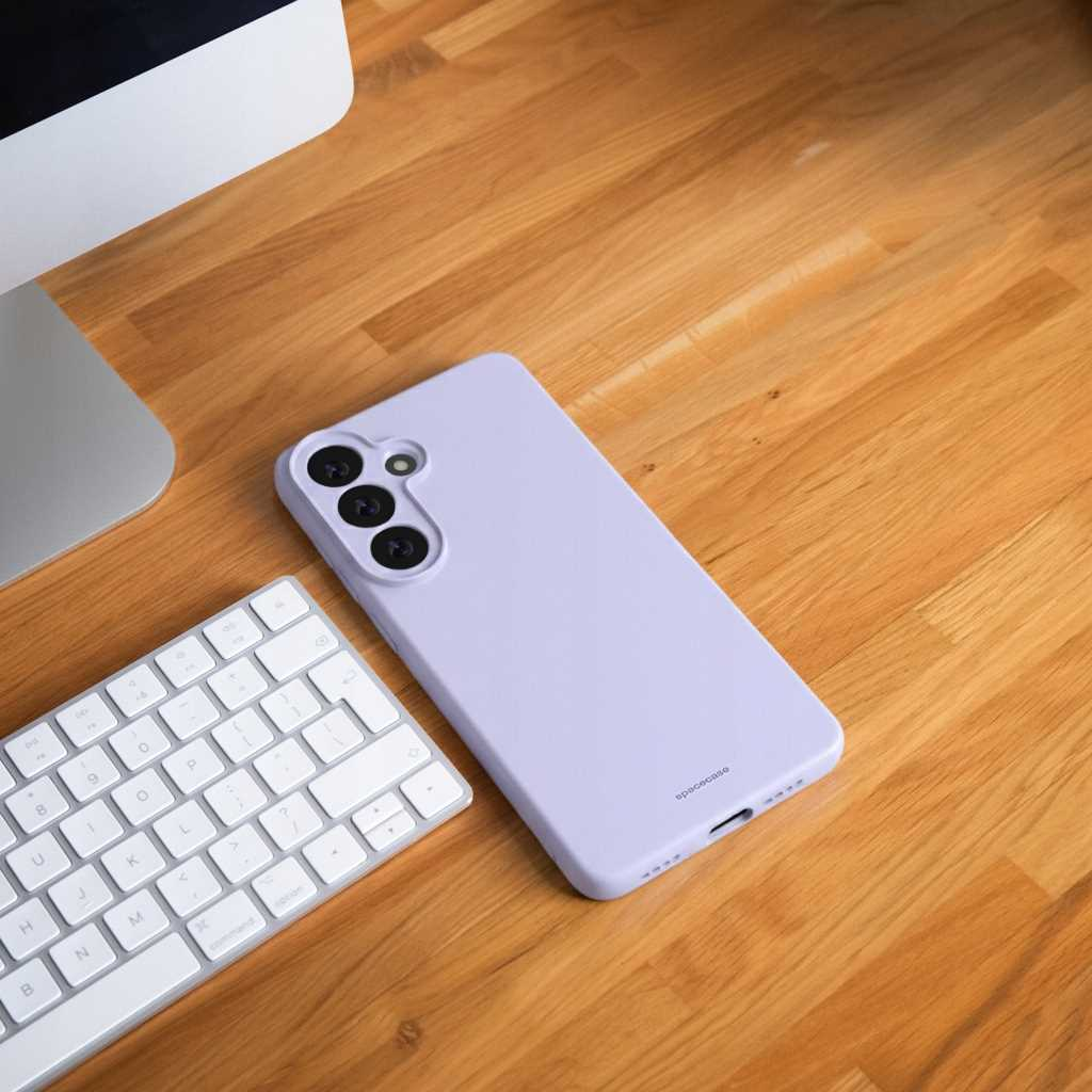 Fioletowe etui na telefon leży obok klawiatury na drewnianym biurku.