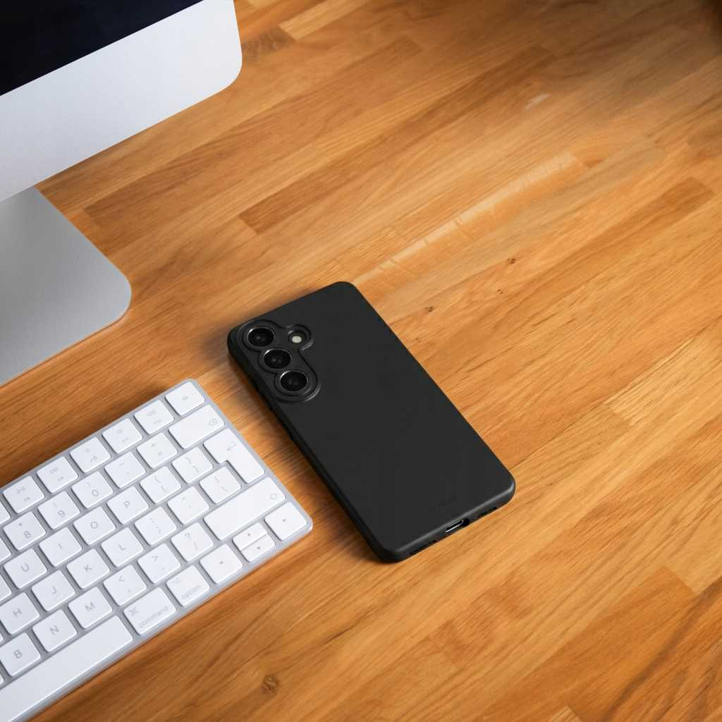 Czarny smartfon leży obok białej klawiatury na drewnianym biurku.