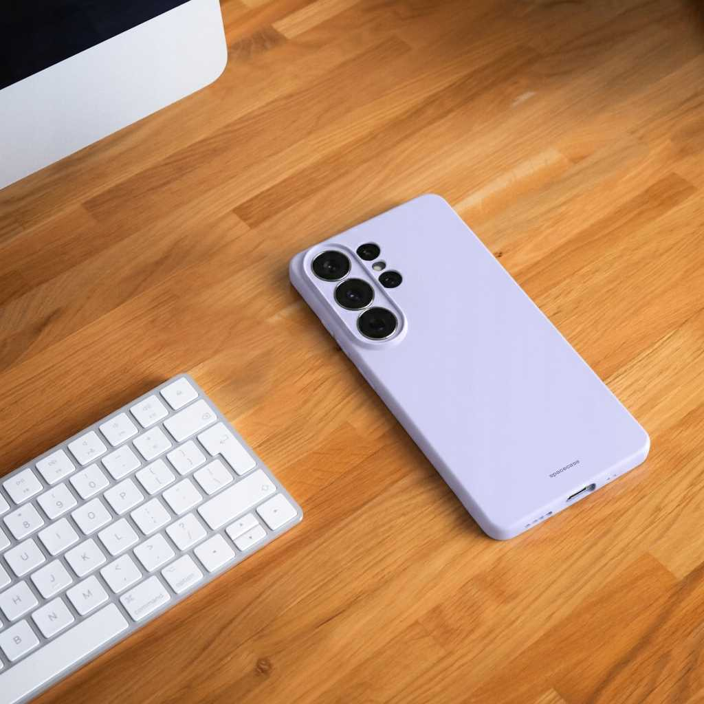 Fioletowe etui na telefon leży obok klawiatury na drewnianym biurku.