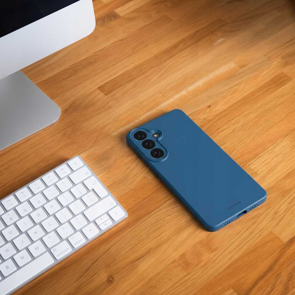 Niebieskie etui na telefon leży obok klawiatury i monitora.