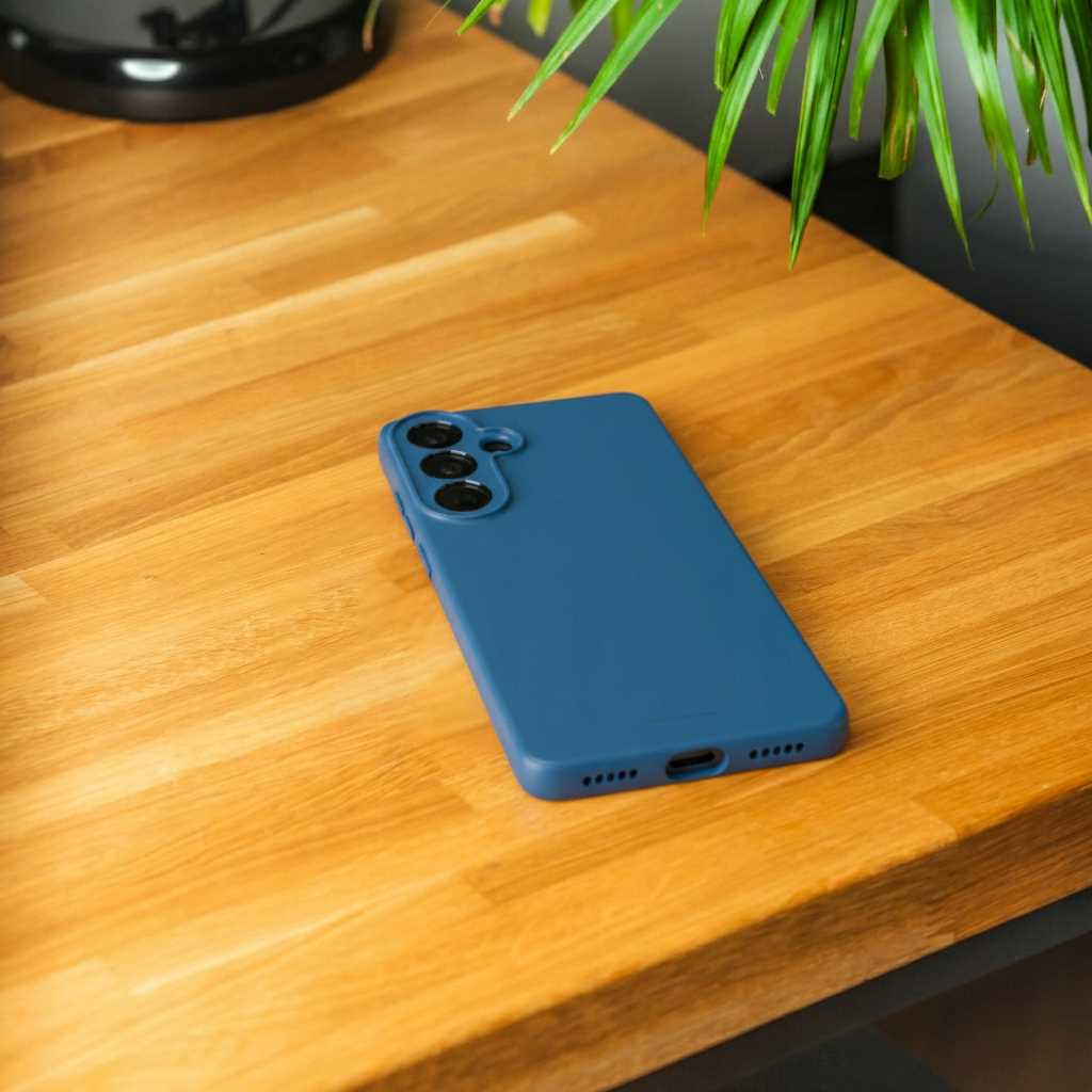 Niebieskie etui na telefon z trzema aparatami leży na drewnianym stole. Widoczne są zielone liście.