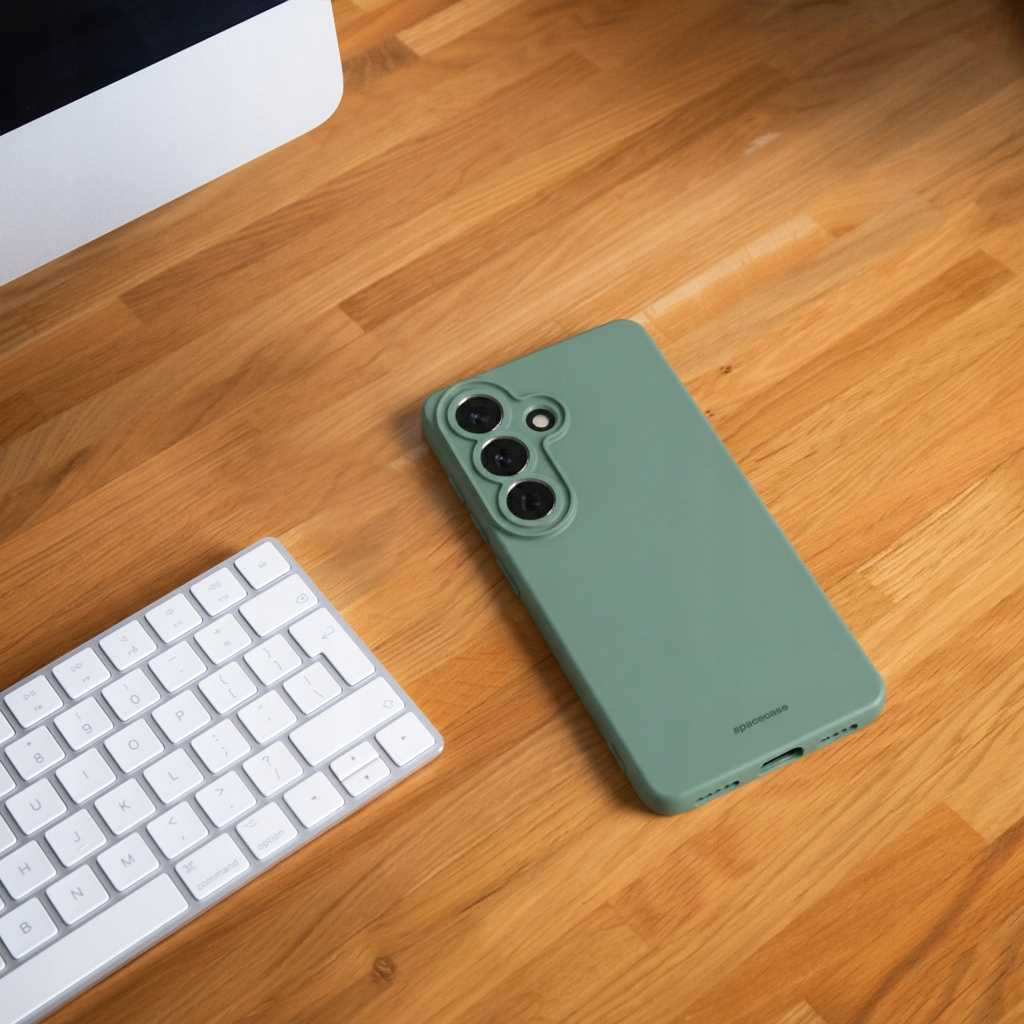 Zielone etui na telefon leży obok klawiatury na drewnianym stole.
