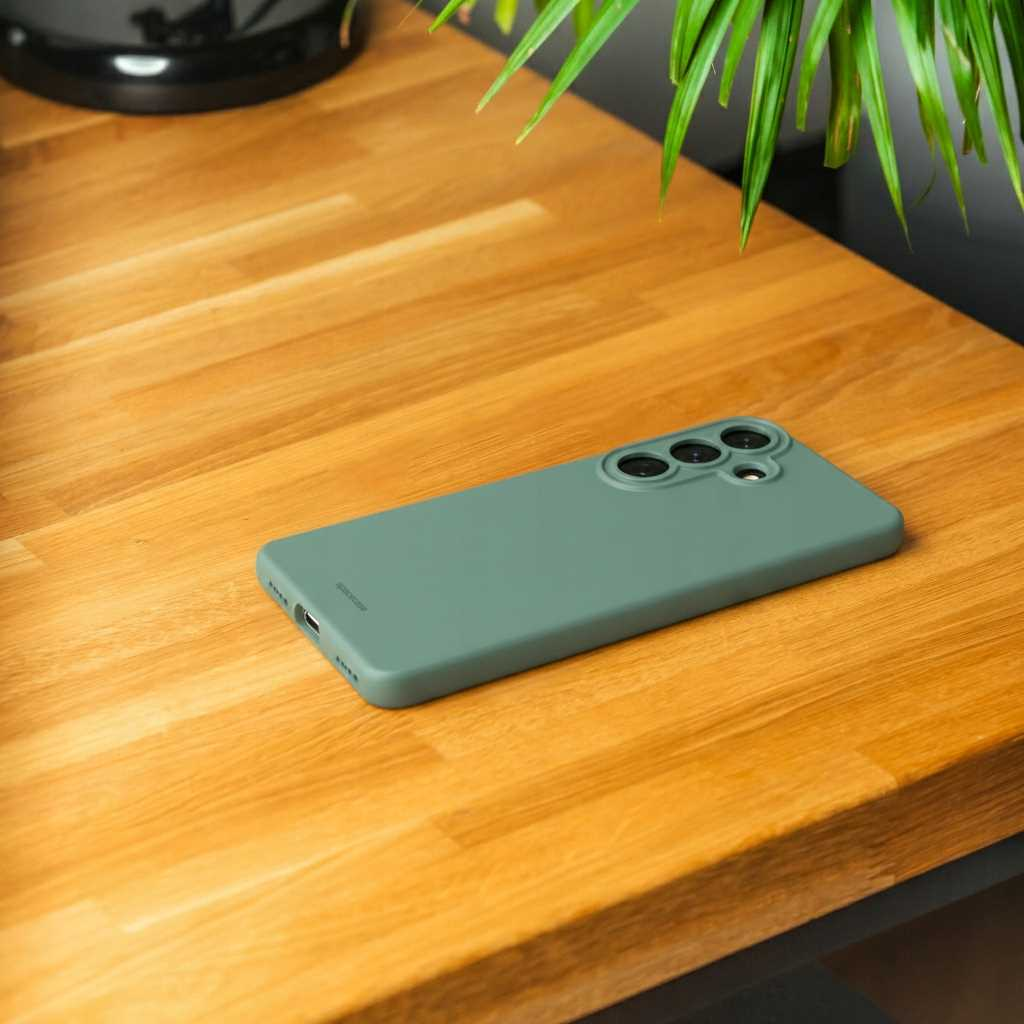 Zielony telefon z modułem aparatu leży na drewnianym stole obok rośliny.