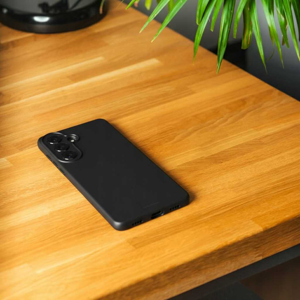 Czarny smartfon leży na drewnianym stole, obok roślina.