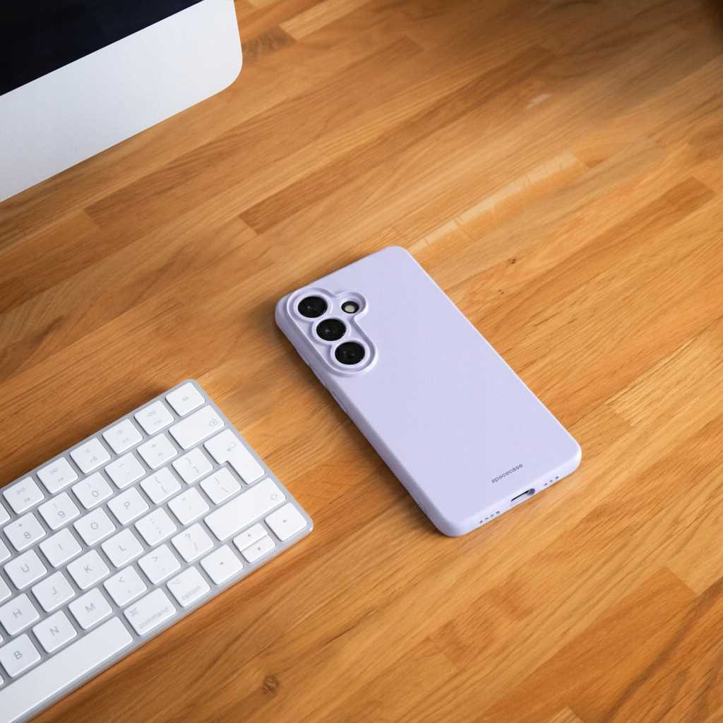 Fioletowy telefon z trzema aparatami obok białej klawiatury na drewnie.