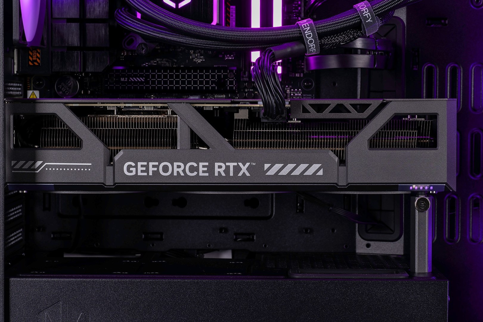 Zbliżenie ciemnoszarej karty graficznej Geforce RTX w obudowie komputera, z fioletowym podświetleniem.