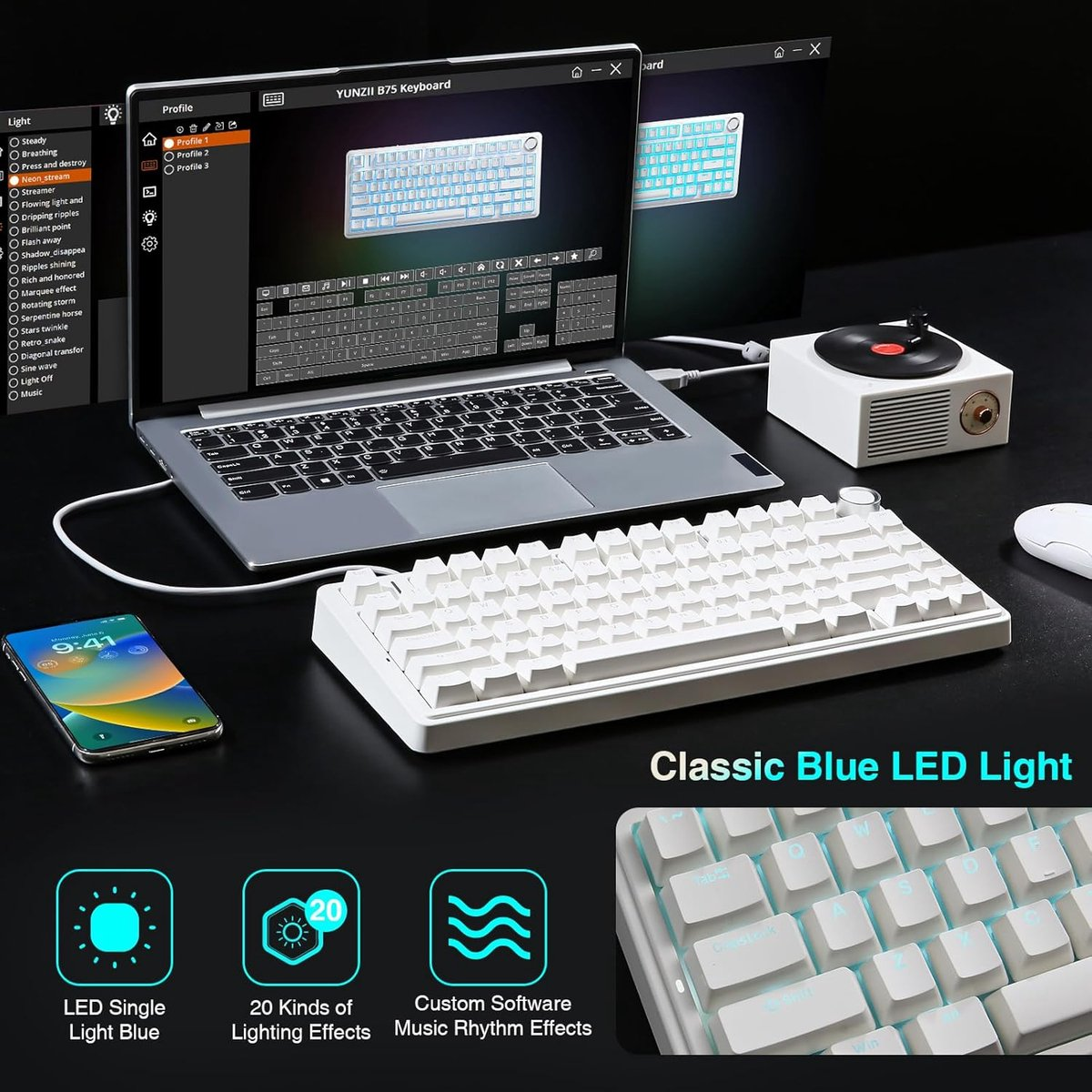 Un clavier blanc, un ordinateur portable, un smartphone et un petit tourne-disque sur une table noire.
