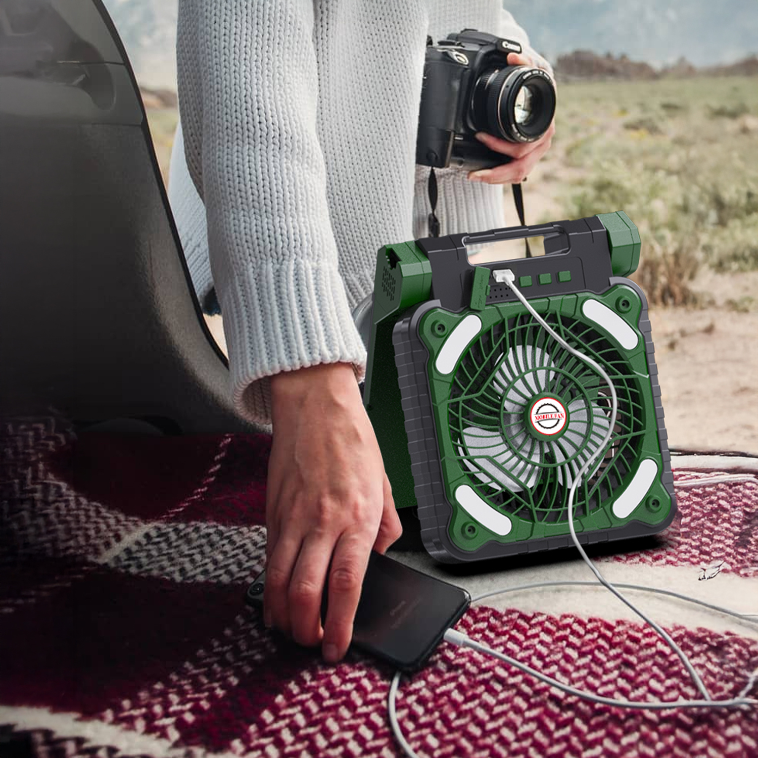Una persona carica un telefono su un ventilatore verde, seduta su una coperta.
