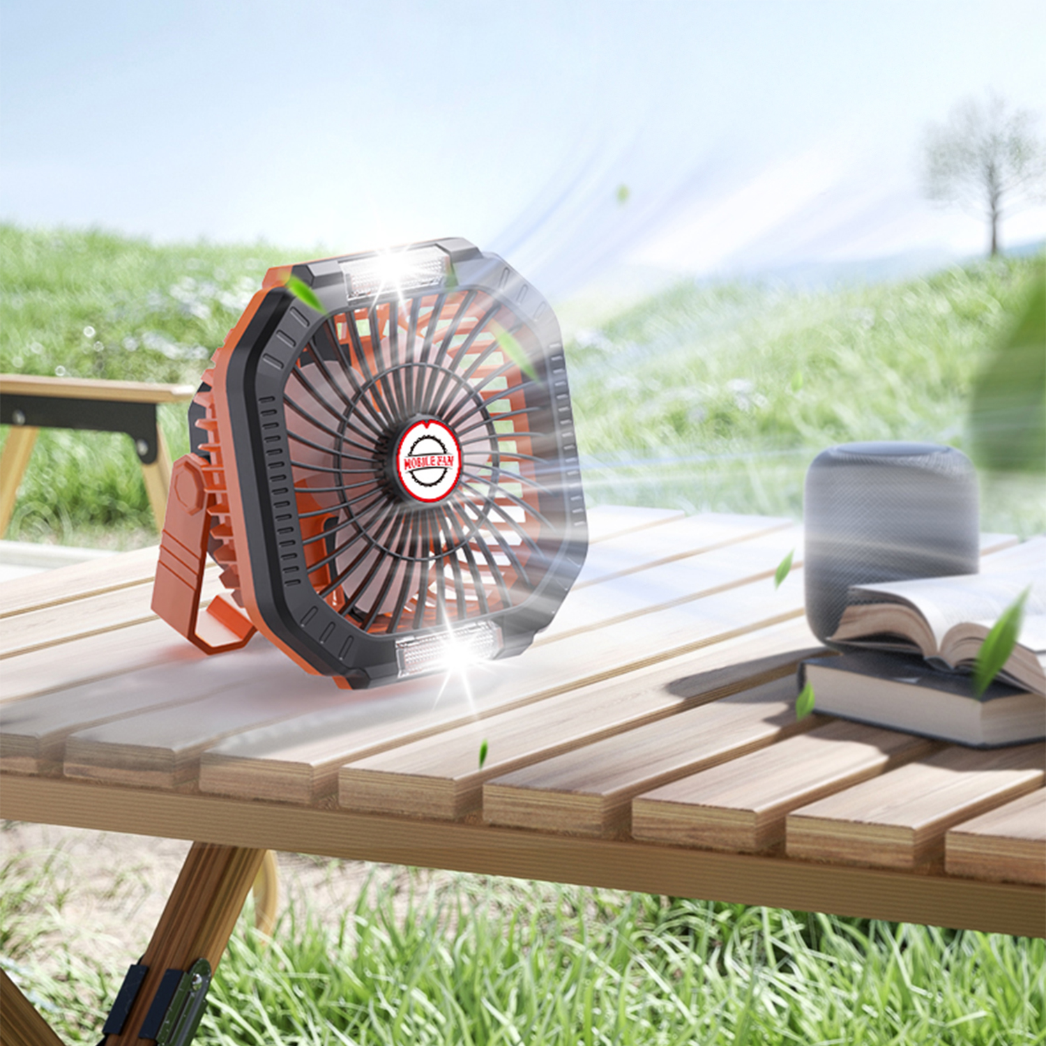 Un ventilatore arancione su un tavolo di legno con libri e altoparlante all'aperto.