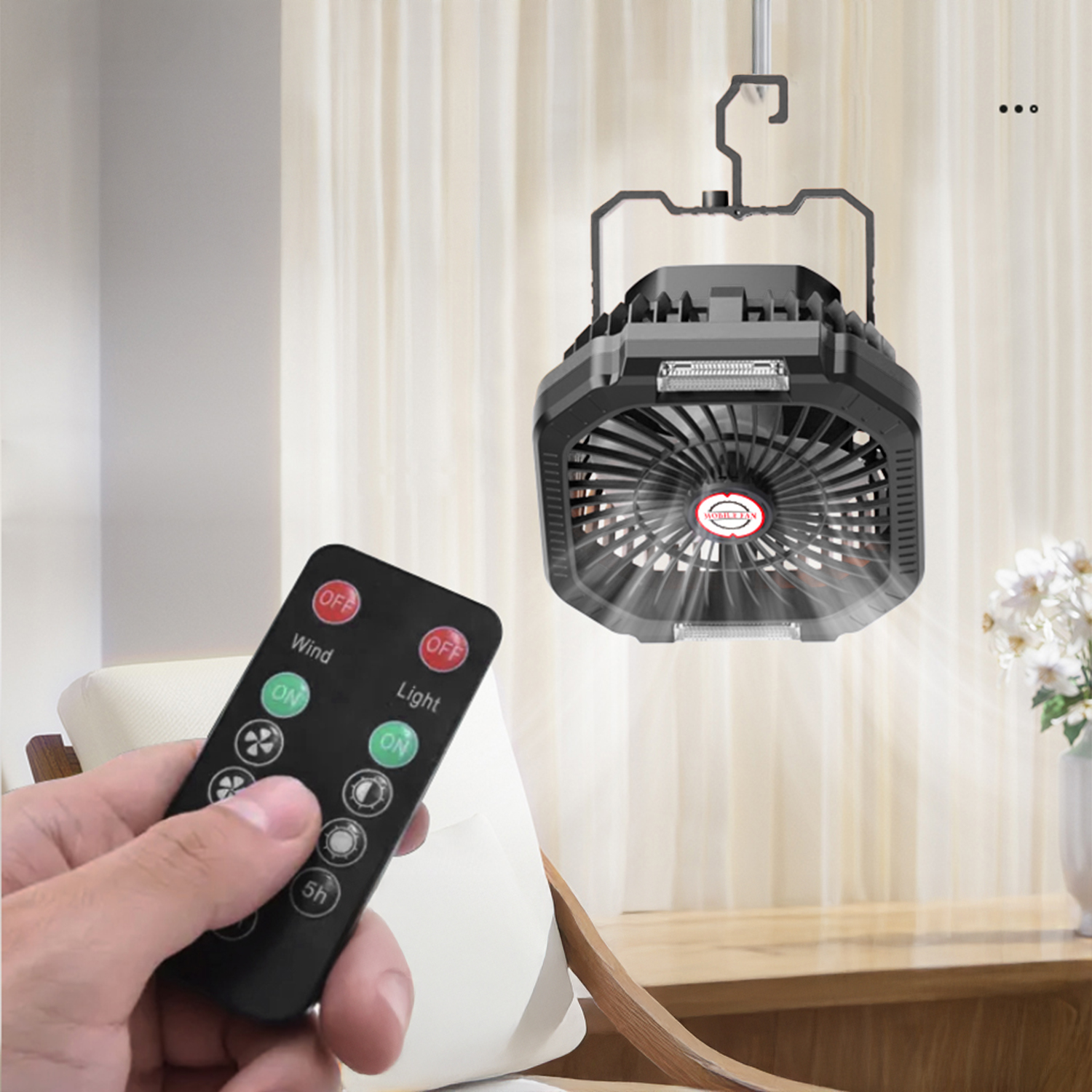Una mano tiene un telecomando nero con pulsanti per vento e luce. Un ventilatore è appeso sullo sfondo.