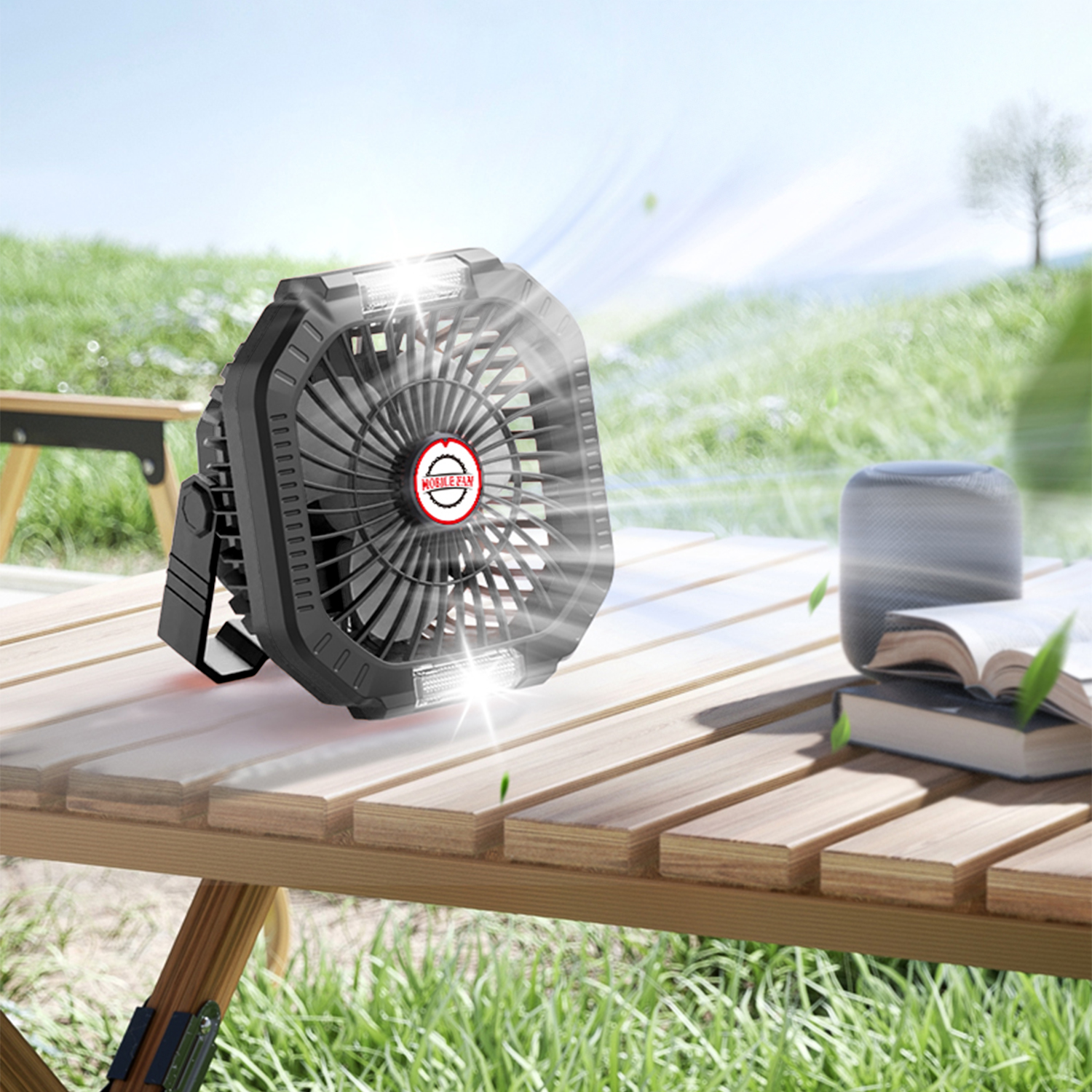 Un ventilatore nero su un tavolo di legno accanto a libri e un altoparlante all'aperto.