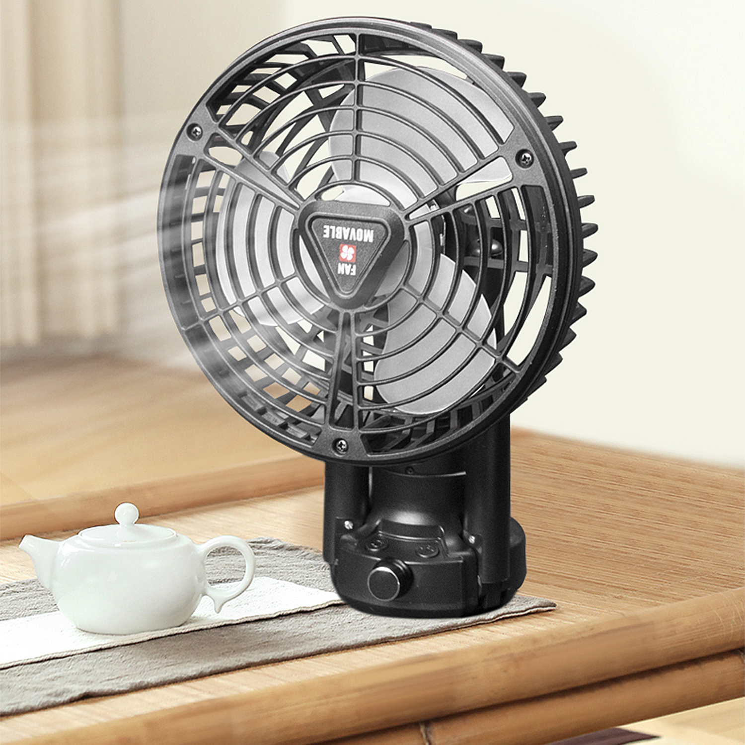 Un ventilatore nero soffia aria su una piccola teiera bianca su un tavolo di legno.