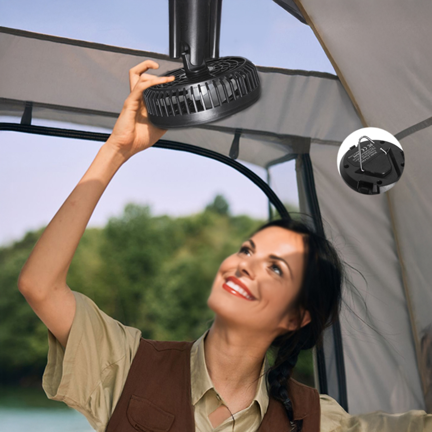 Donna installa una ventola portatile nera dentro una tenda. Alberi e cielo visibili all'esterno.
