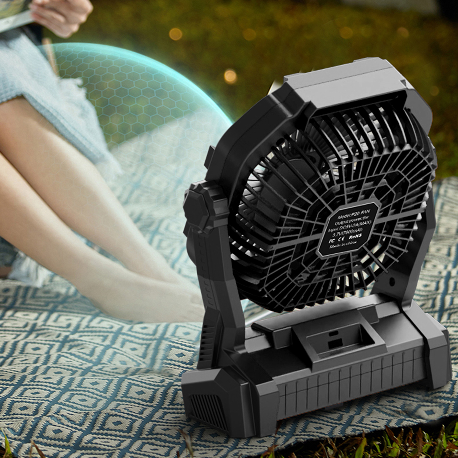 Un ventilatore nero su una coperta accanto alle gambe di una persona.