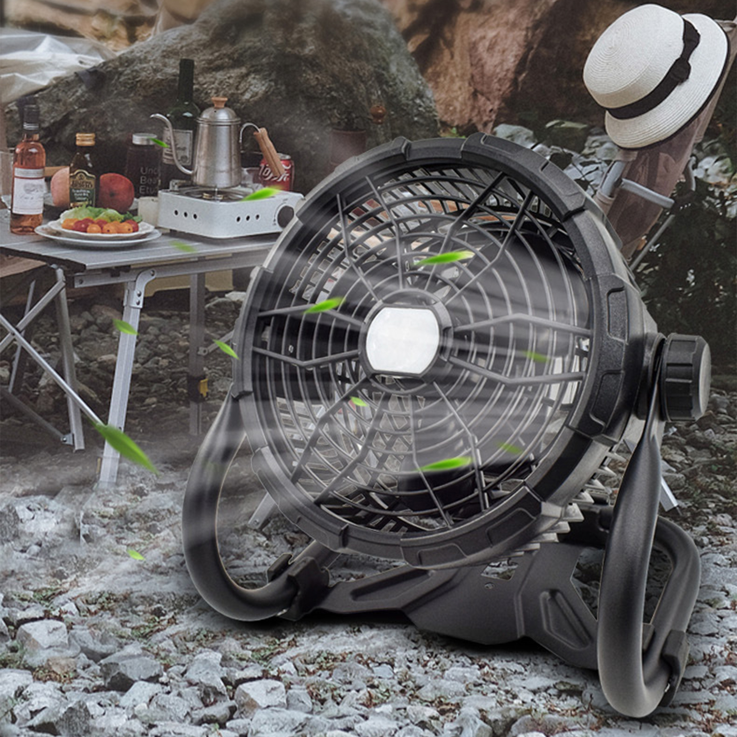 Un ventilatore portatile nero funziona all'aperto su una superficie rocciosa vicino a un tavolo da picnic con cibo e bevande.