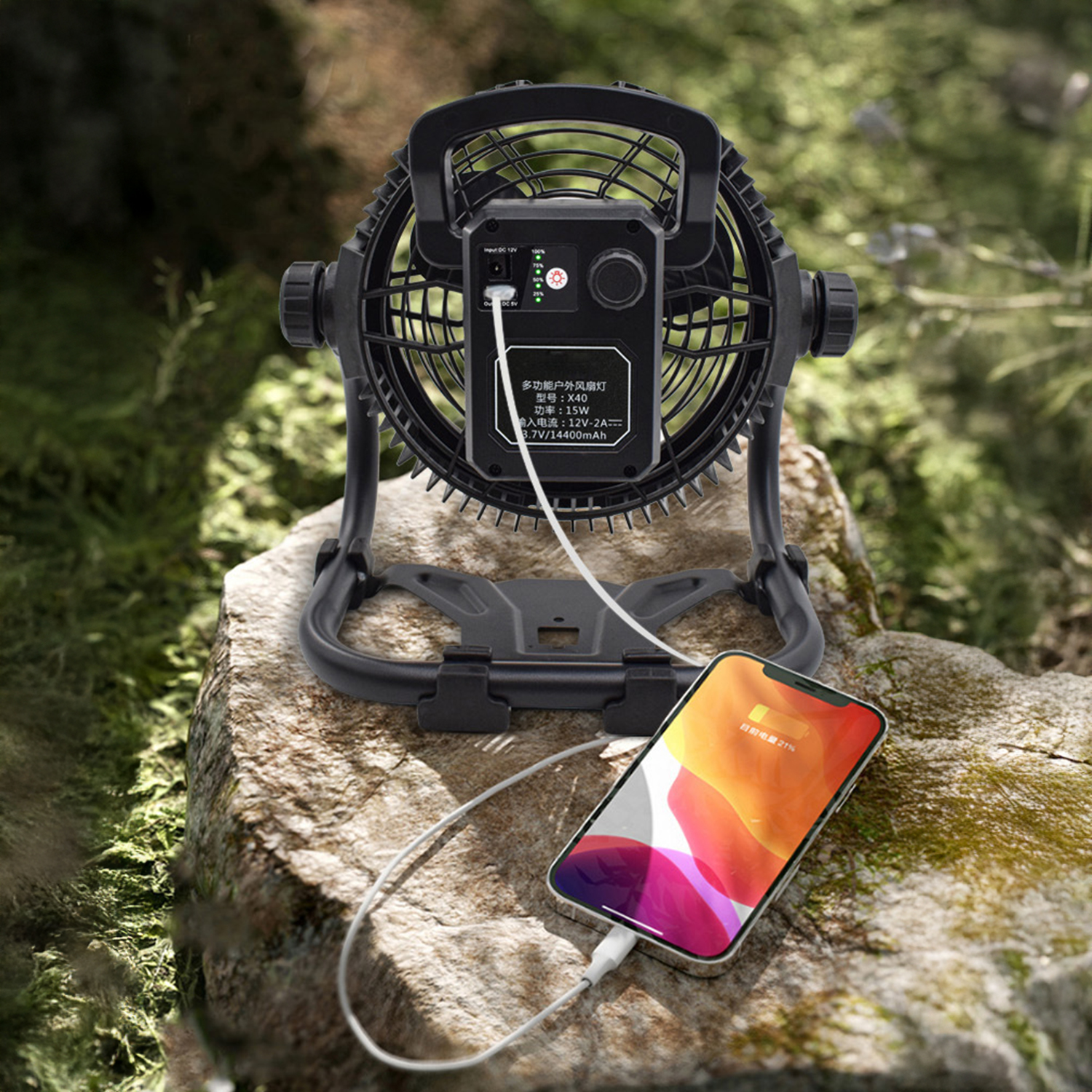 Un ventilatore nero da esterno carica uno smartphone su una roccia all'aperto.