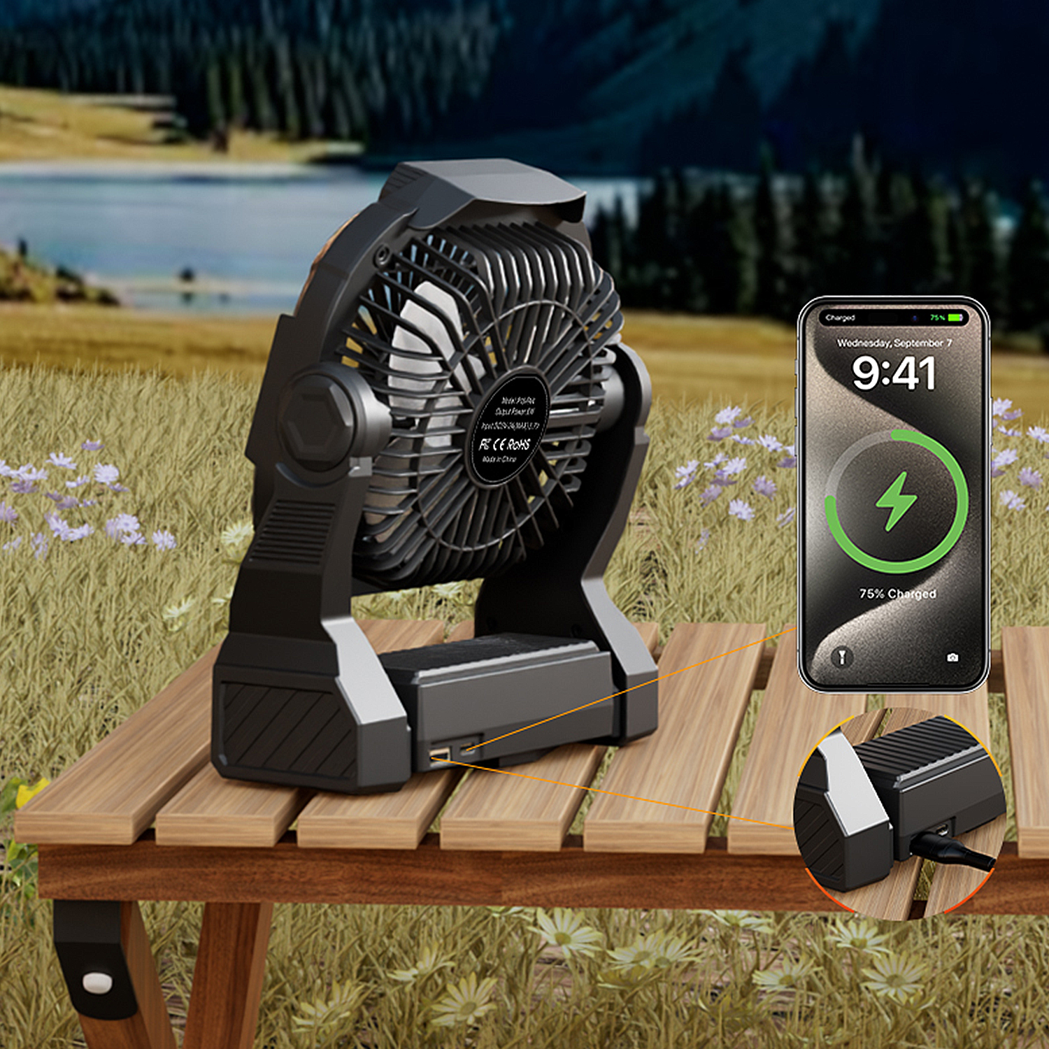 Ventilatore portatile nero su tavolo di legno, carica telefono. Sfondo lago e foresta.
