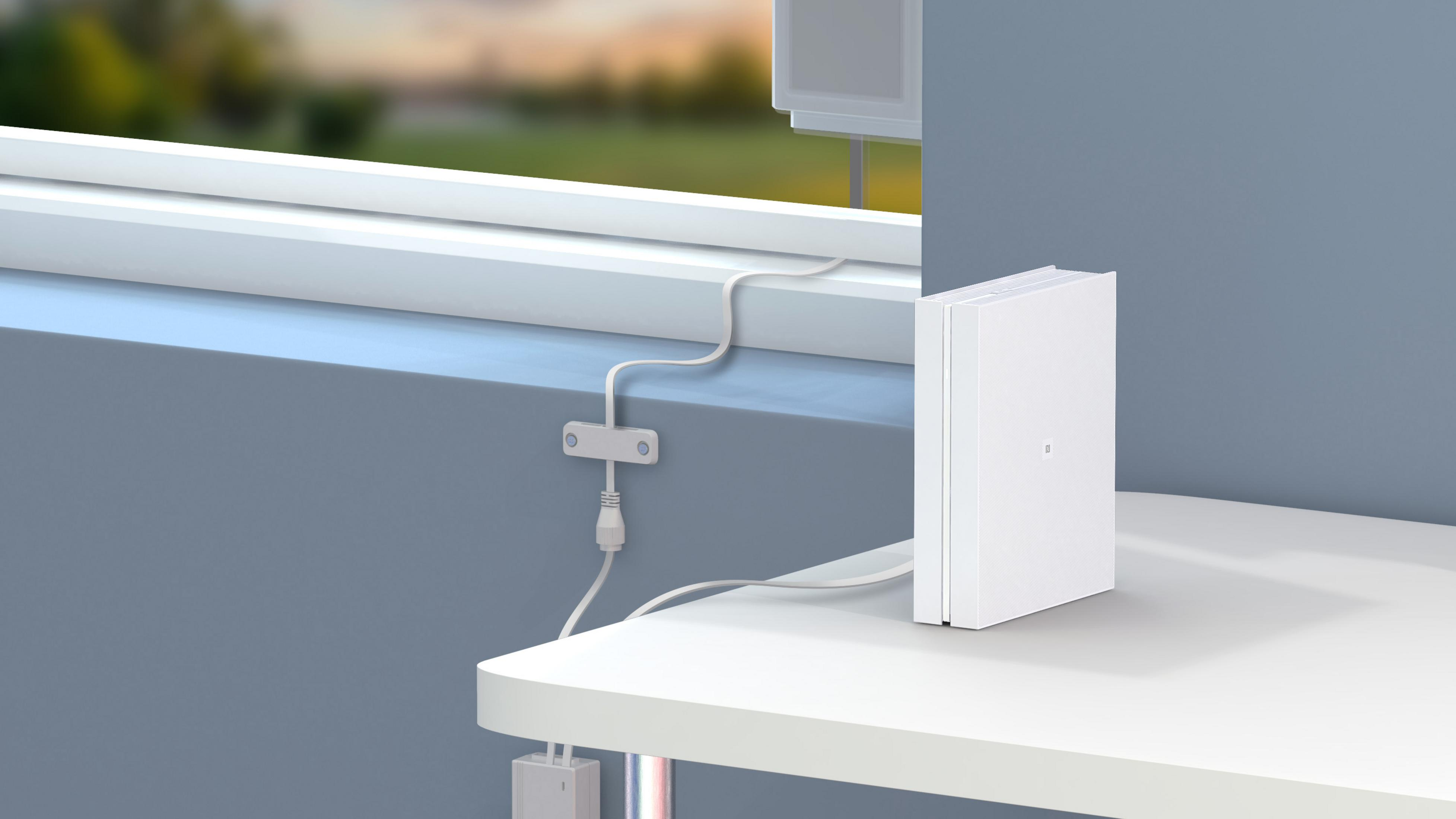 Białe urządzenie stoi na stole obok okna z widokiem na zieleń.