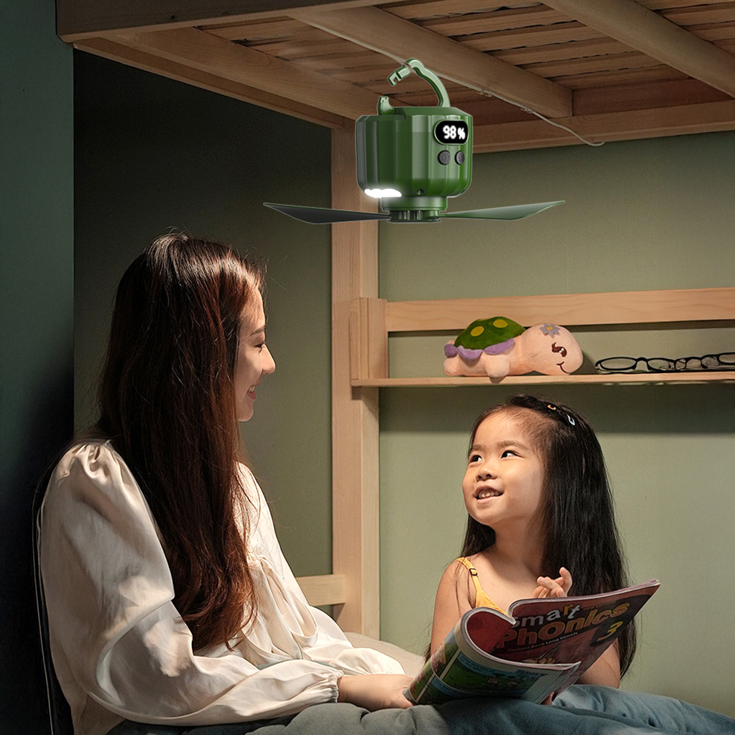 Una donna e un bambino leggono a letto. Un ventilatore verde pende sopra.
