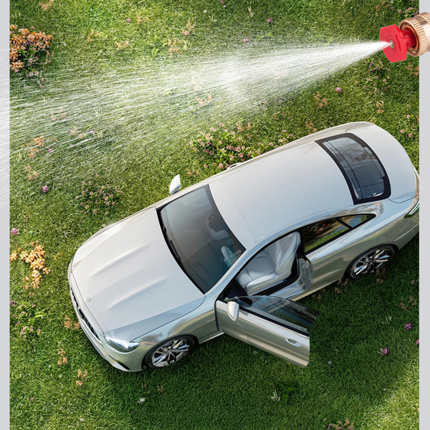 Silbernes Auto wird auf grünem Rasen von einem Gartenschlauch mit Wasser bespritzt.