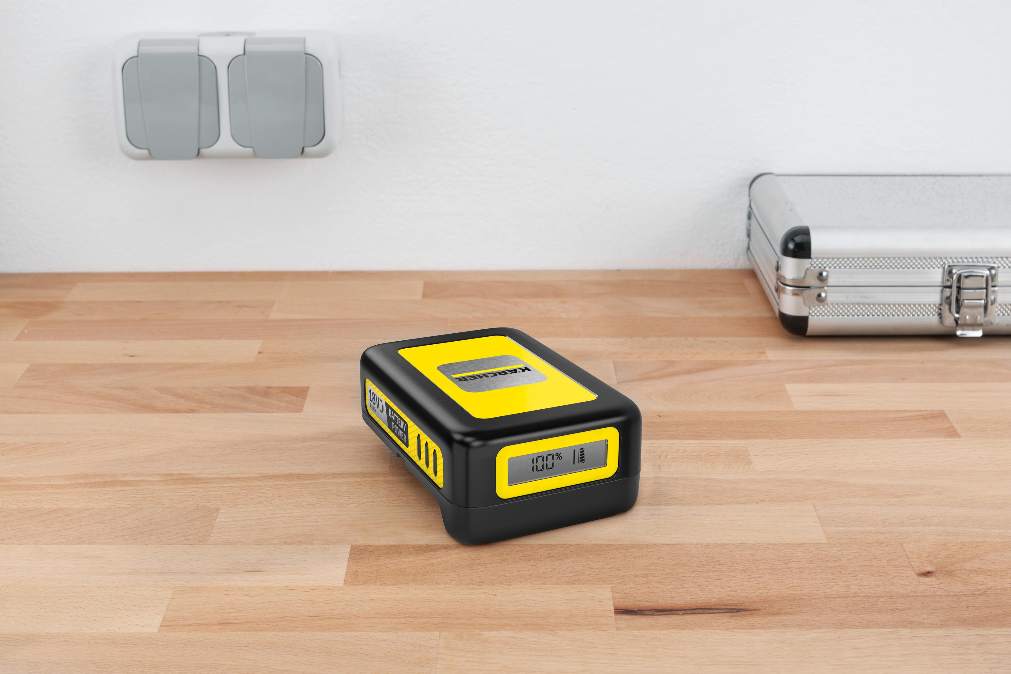 Żółta bateria Karcher 100% na drewnianym stole. Po prawej metalowa walizka.