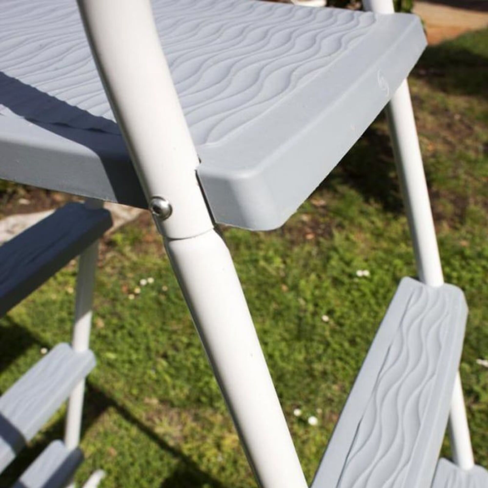 Patas de escalera blancas con peldaños grises con patrón de ondas al aire libre.