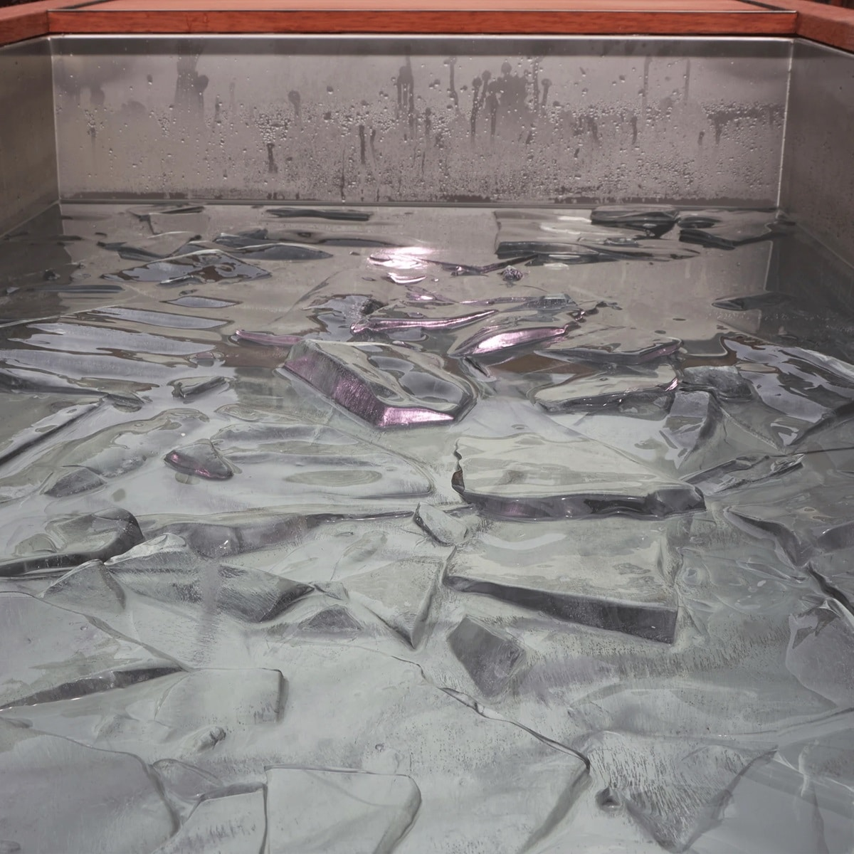 Trozos de hielo flotan en agua en un recipiente metálico con borde de madera.