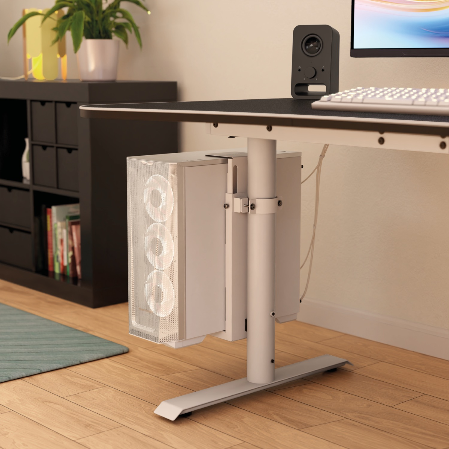 Een witte pc-toren hangt onder een bureau, met een luidspreker en toetsenbord ernaast.