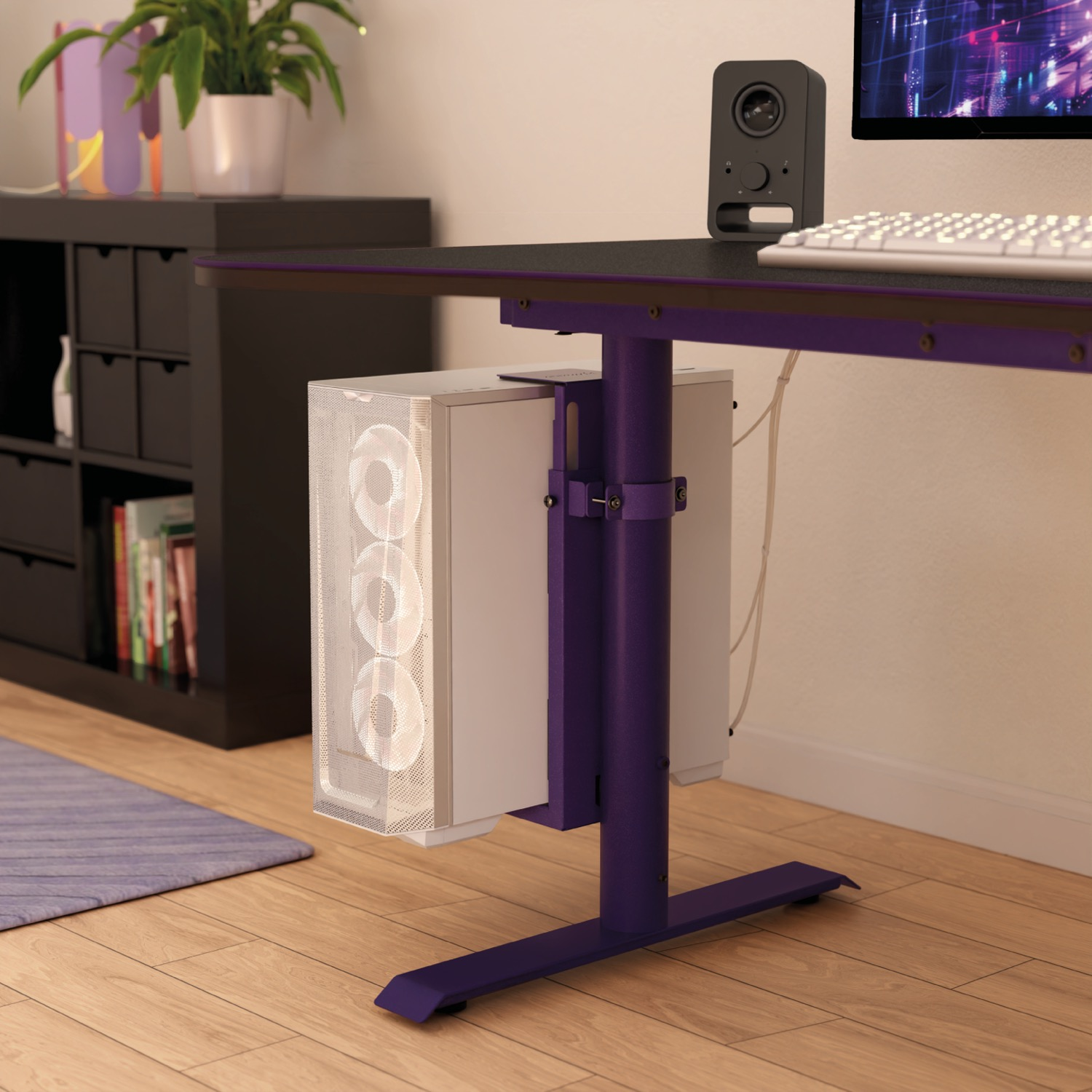 Een witte pc-kast hangt onder een paars bureau, met een zwarte luidspreker ernaast.
