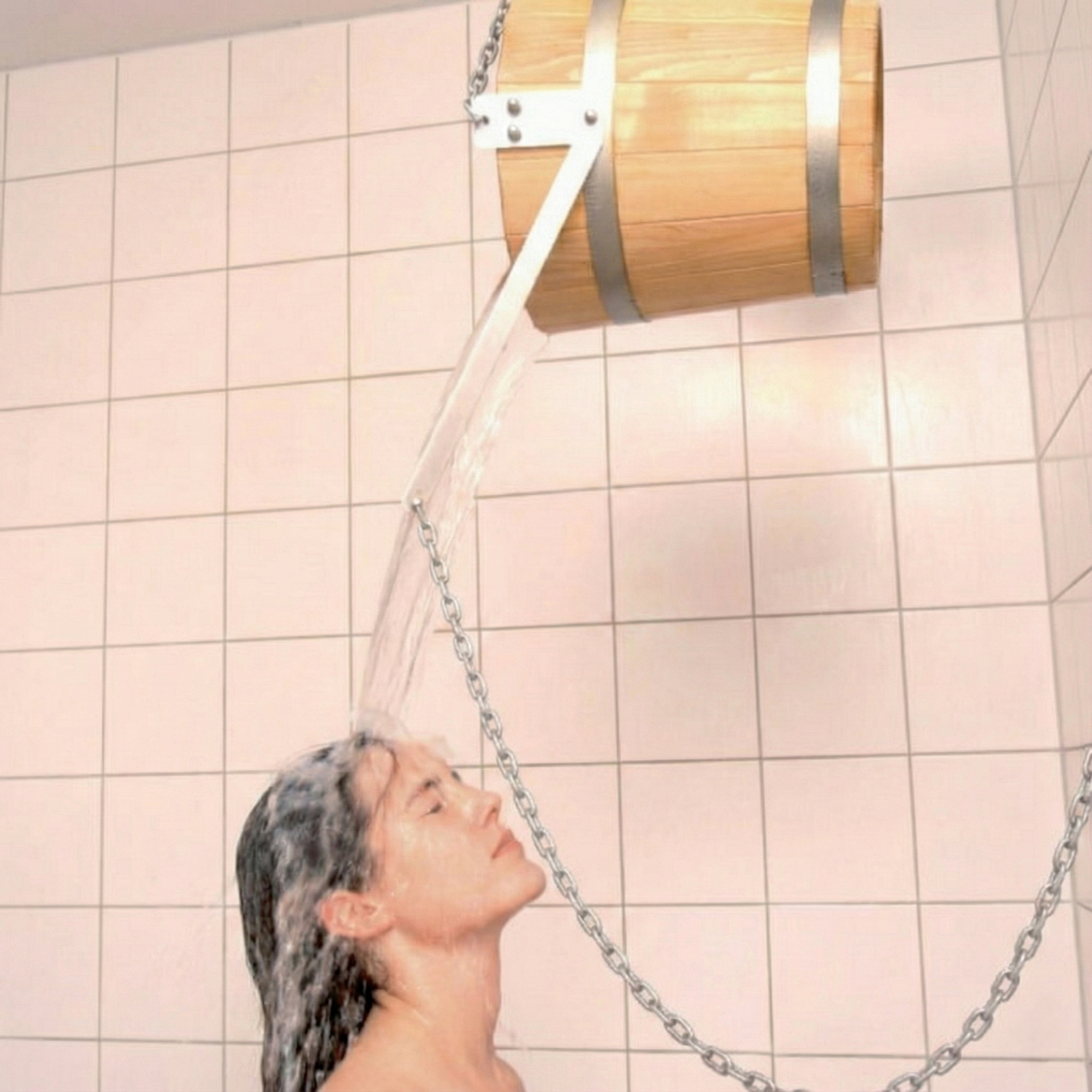Una mujer se para bajo un cubo de madera que le vierte agua.