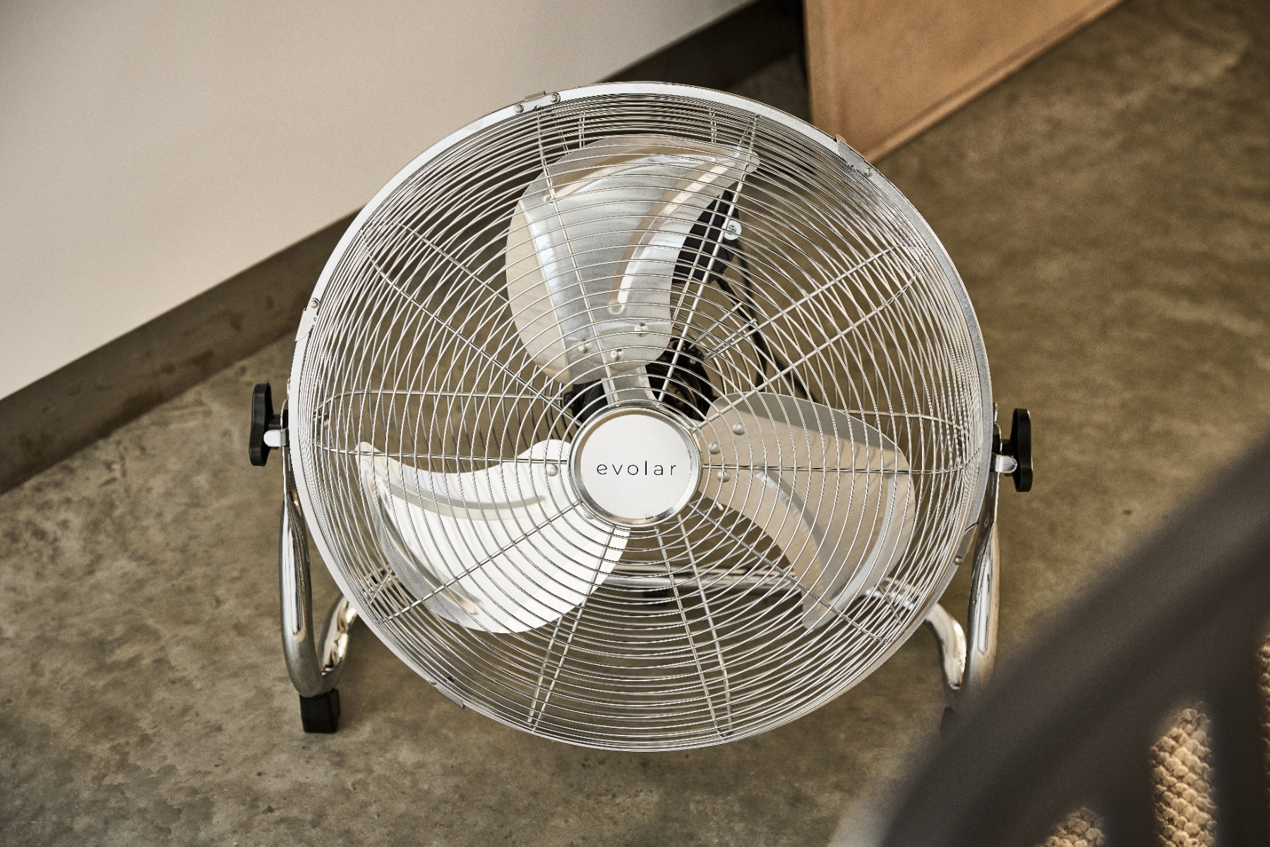 Un ventilatore da terra argentato a tre pale poggia su un pavimento in cemento.