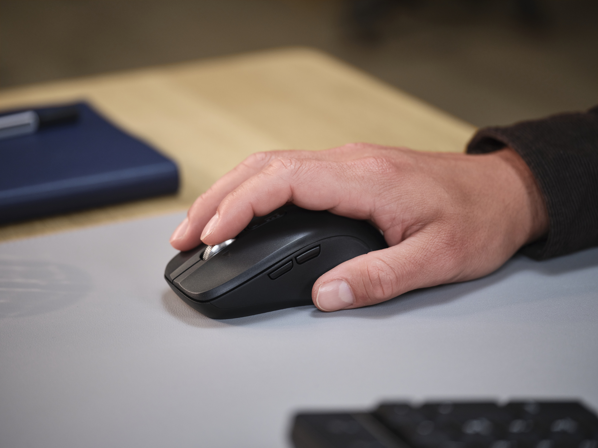 Een hand bedient een zwarte computermuis op een grijze muismat.