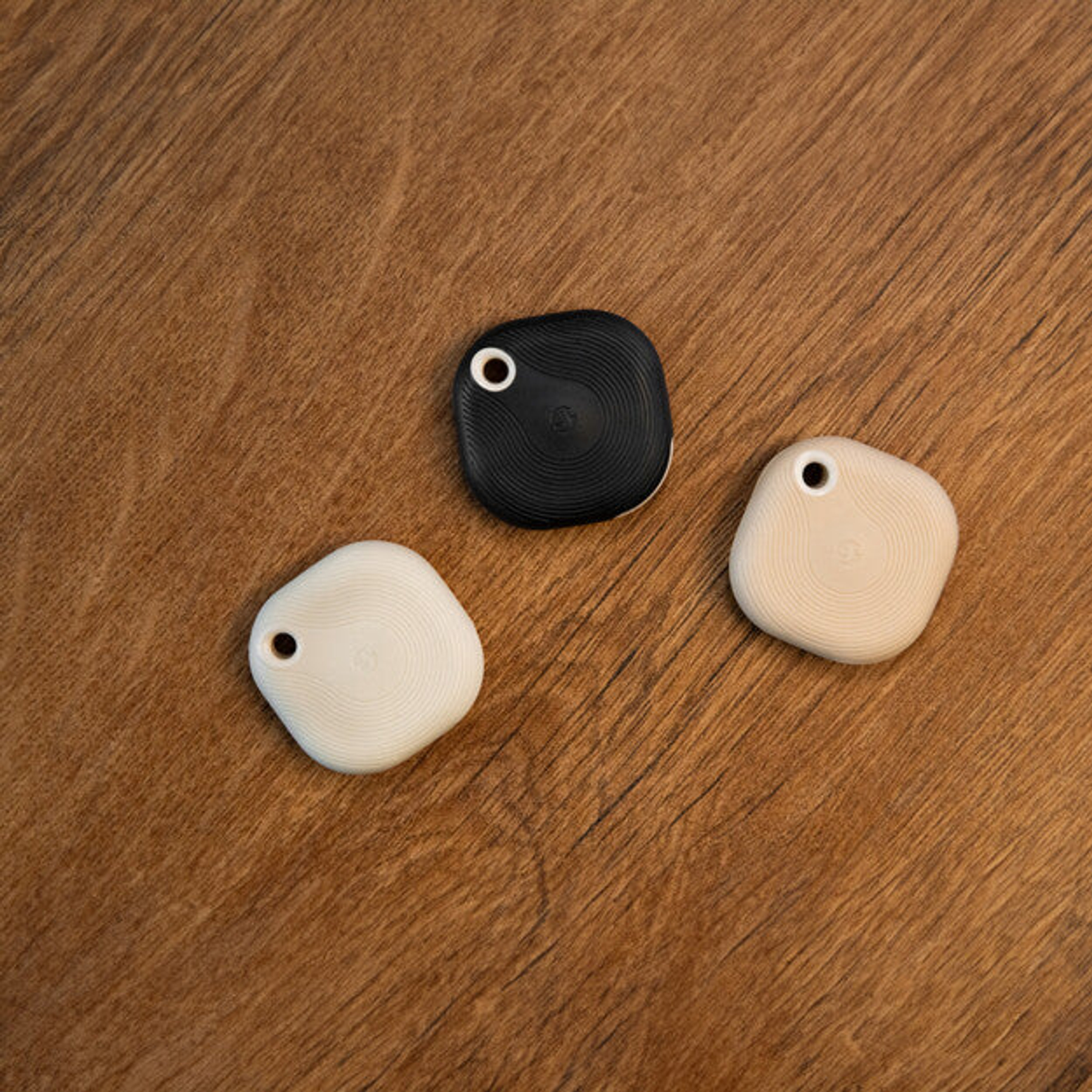 Tre tracker Bluetooth su legno. Due bianchi, uno nero.