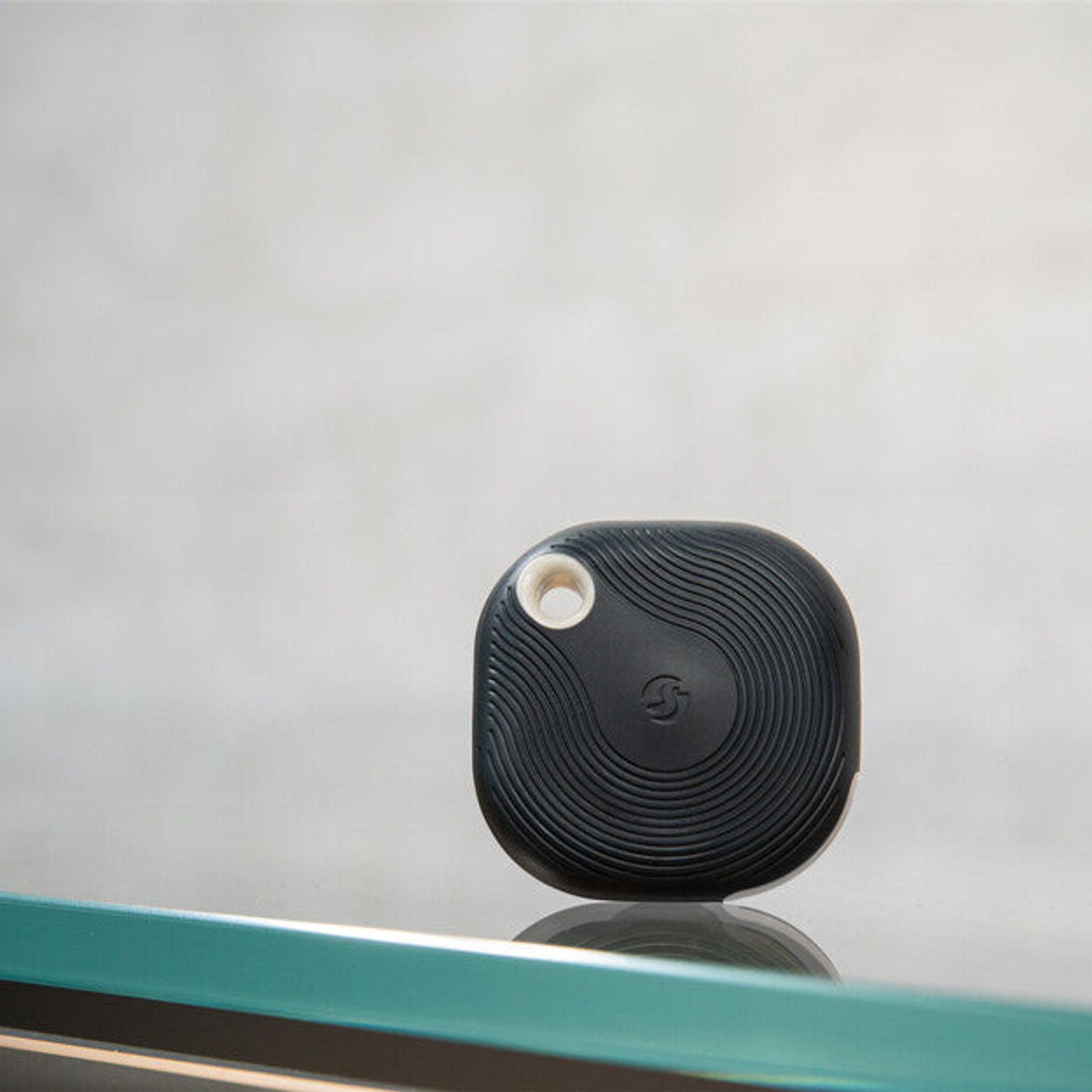 Un localizzatore nero e rotondo con scanalature concentriche e un foro poggia su una superficie di vetro.