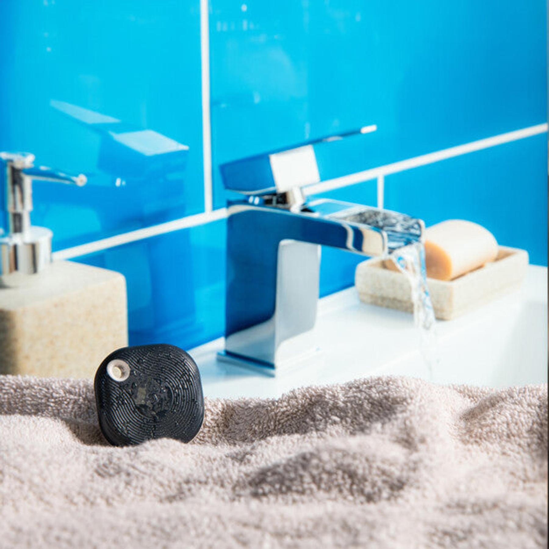 Un dispositivo nero su un asciugamano vicino a un dispenser di sapone e rubinetto.