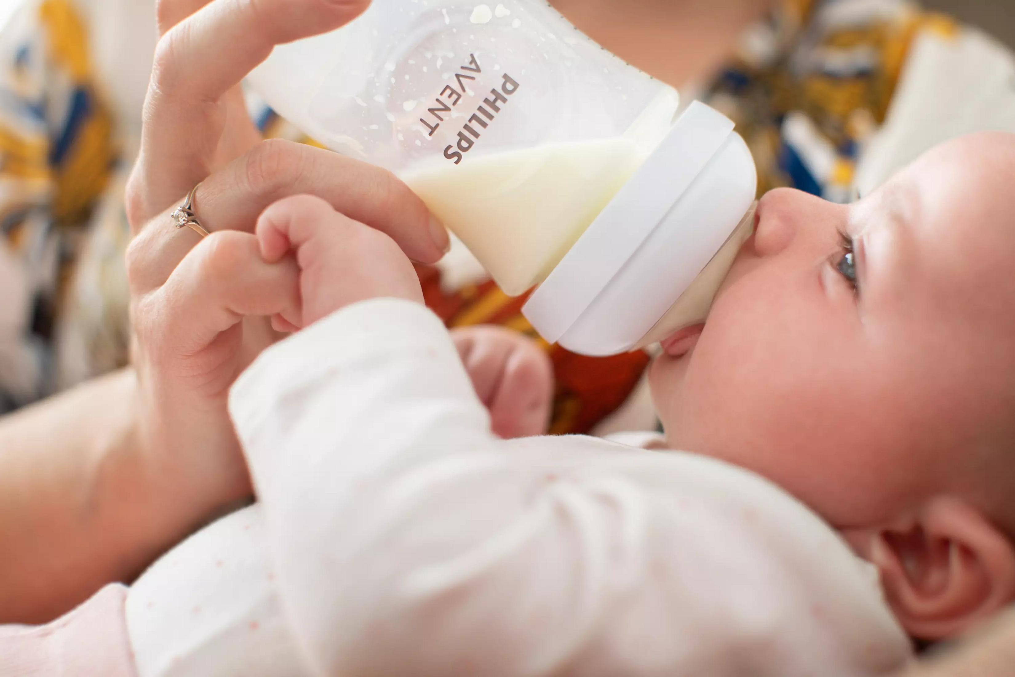 Ein Baby trinkt aus einer Philips Avent Flasche, gehalten von einer Hand.