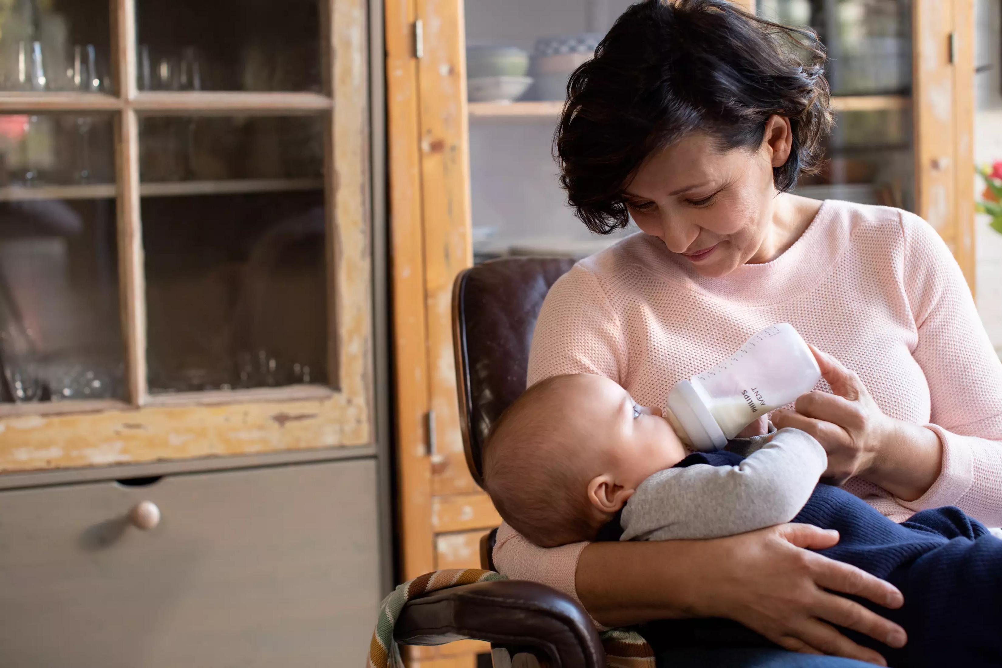 Eine Frau füttert ein Baby mit einer Flasche in einem gemütlichen Raum.