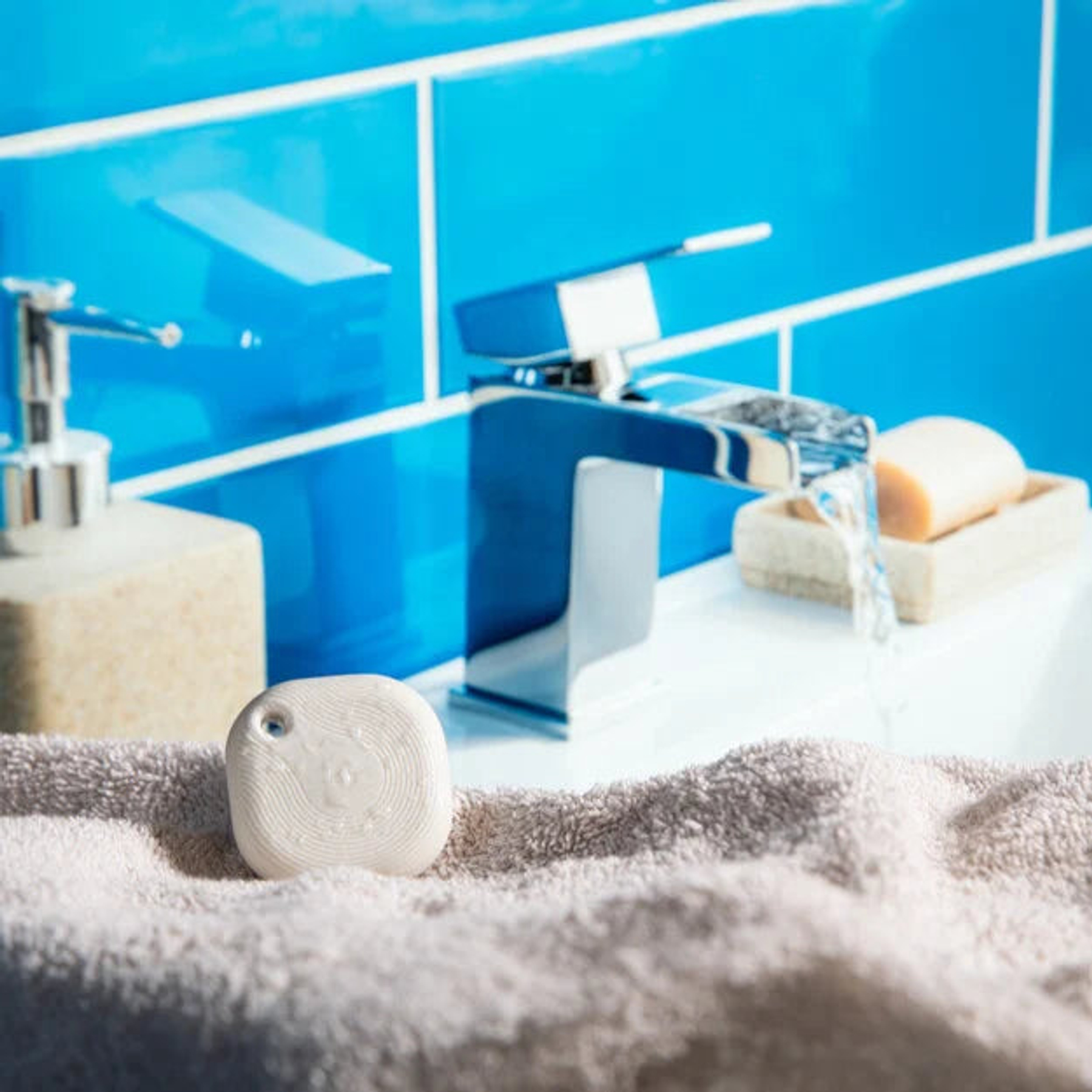 Un tracker bianco poggia su un asciugamano davanti a un rubinetto, dispenser di sapone e sapone.
