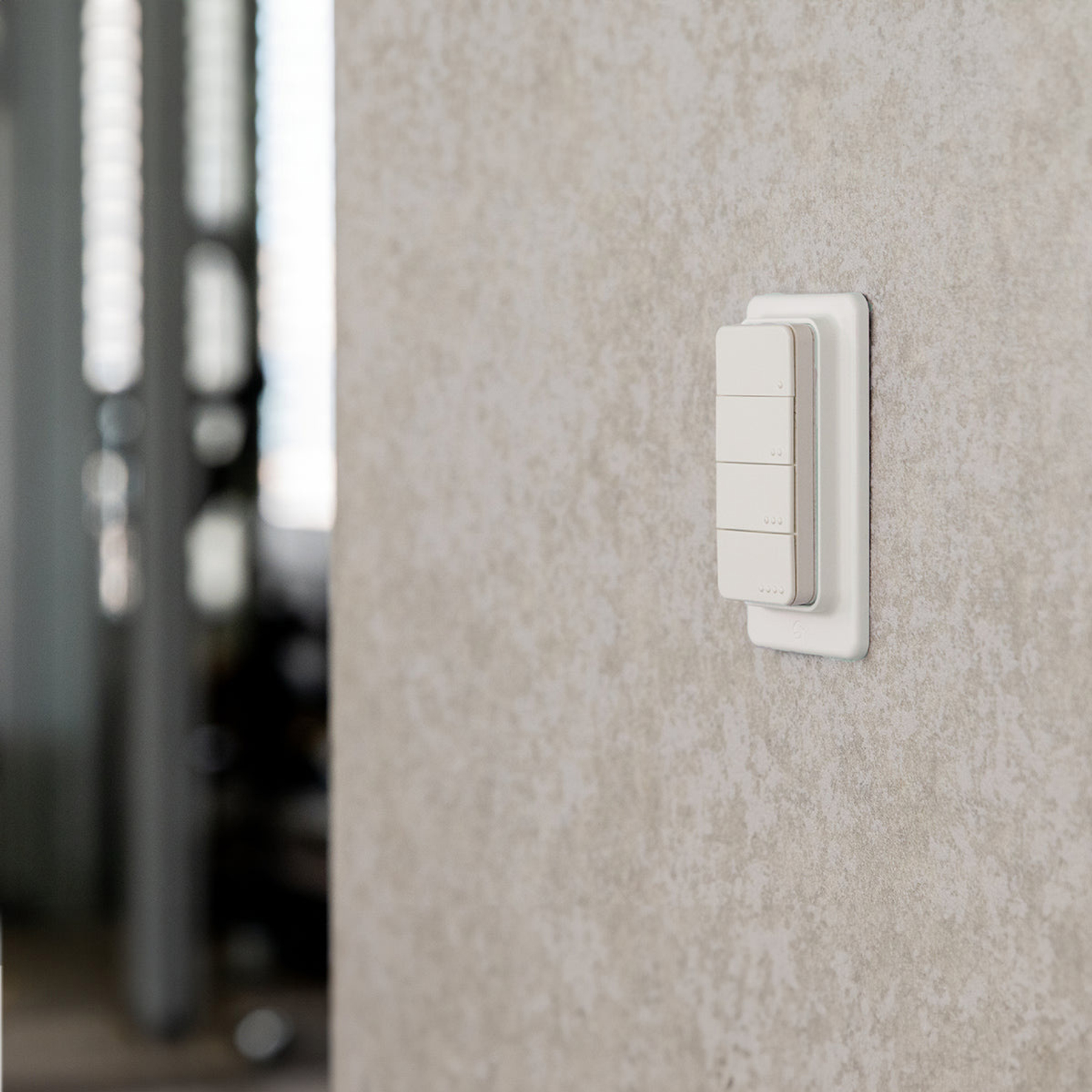 Ein weißer Lichtschalter mit vier Tasten ist an einer strukturierten grauen Wand montiert.