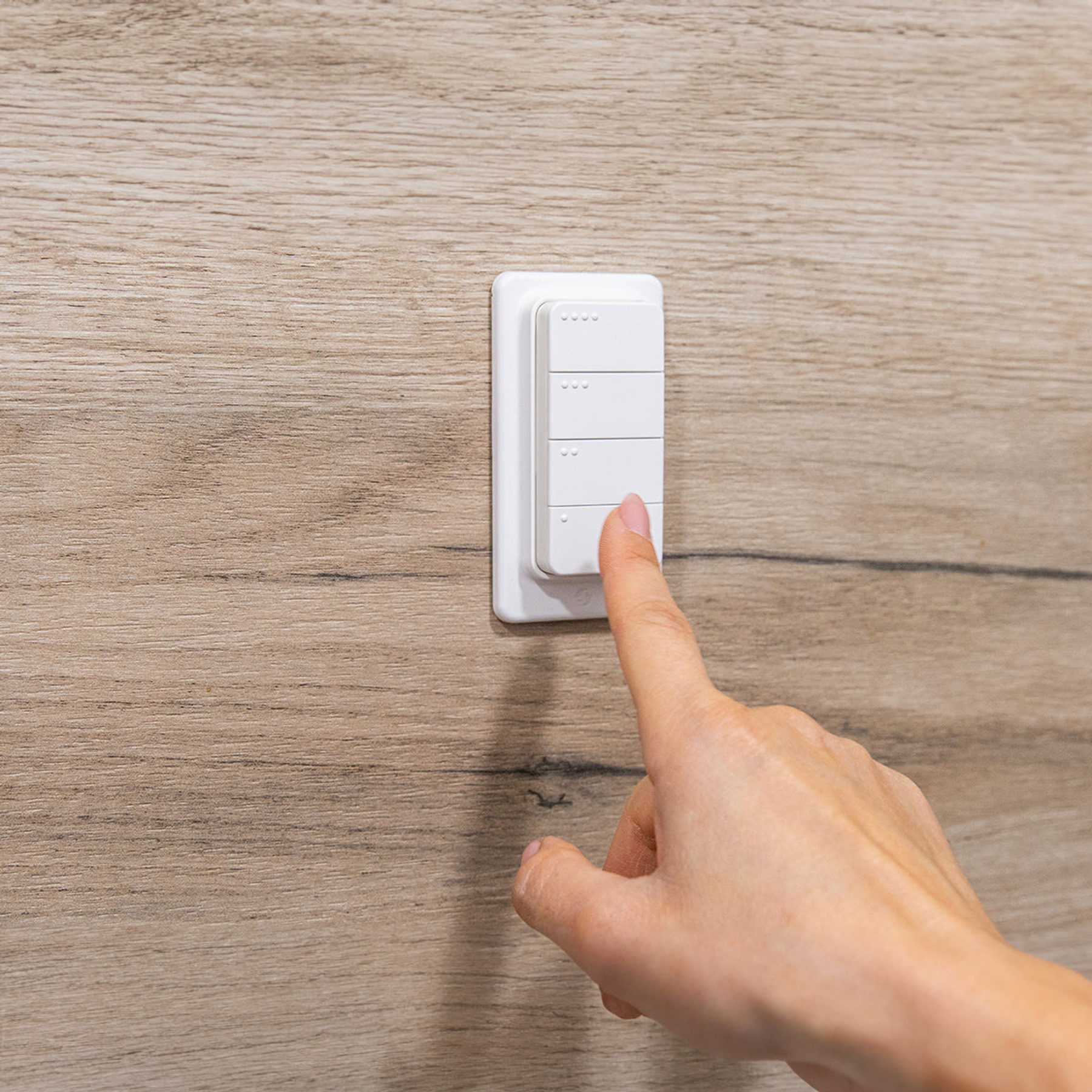 Eine Hand drückt einen weißen Lichtschalter auf hölzerner Wand.