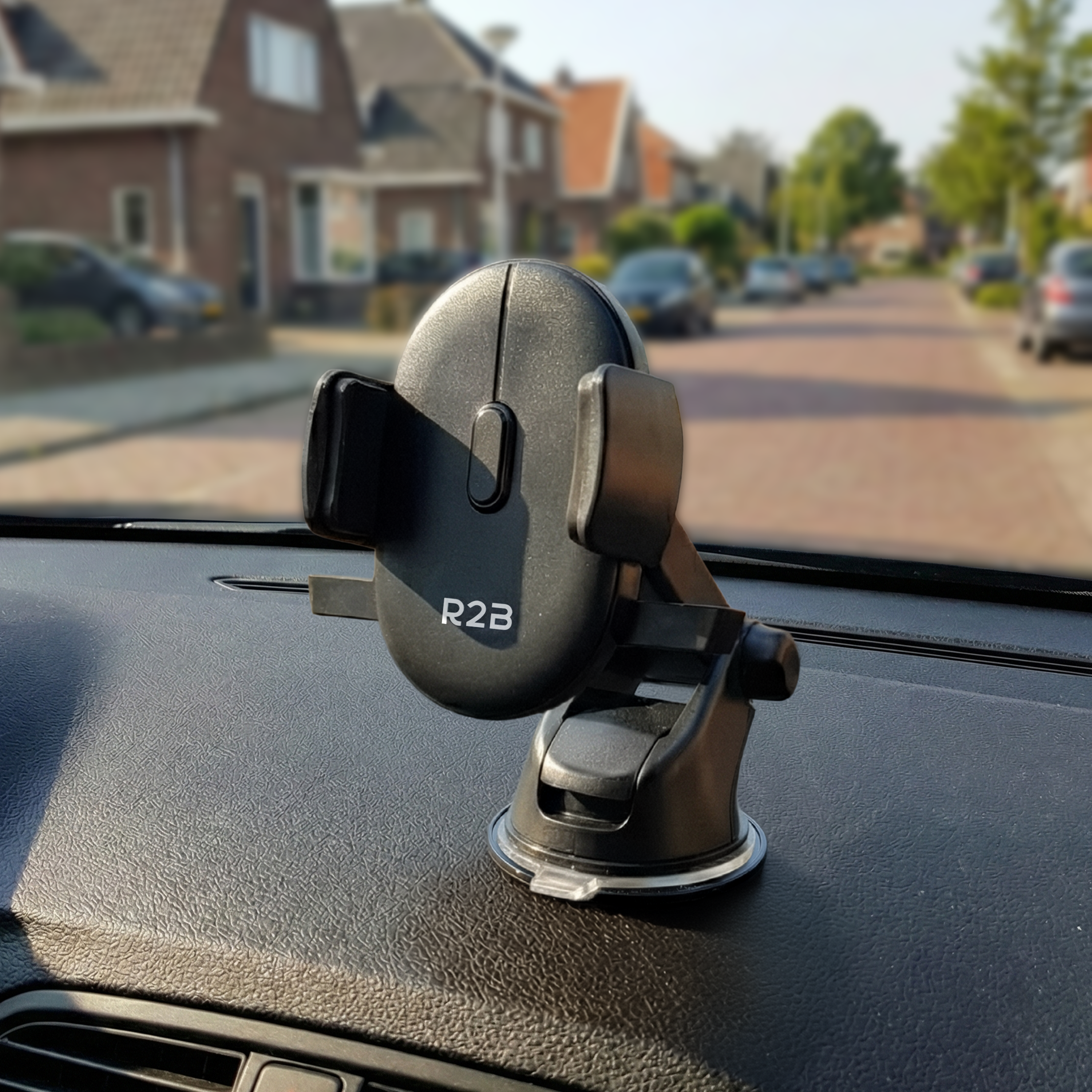 Zwarte telefoonhouder op auto dashboard, met straat en huizen op achtergrond.