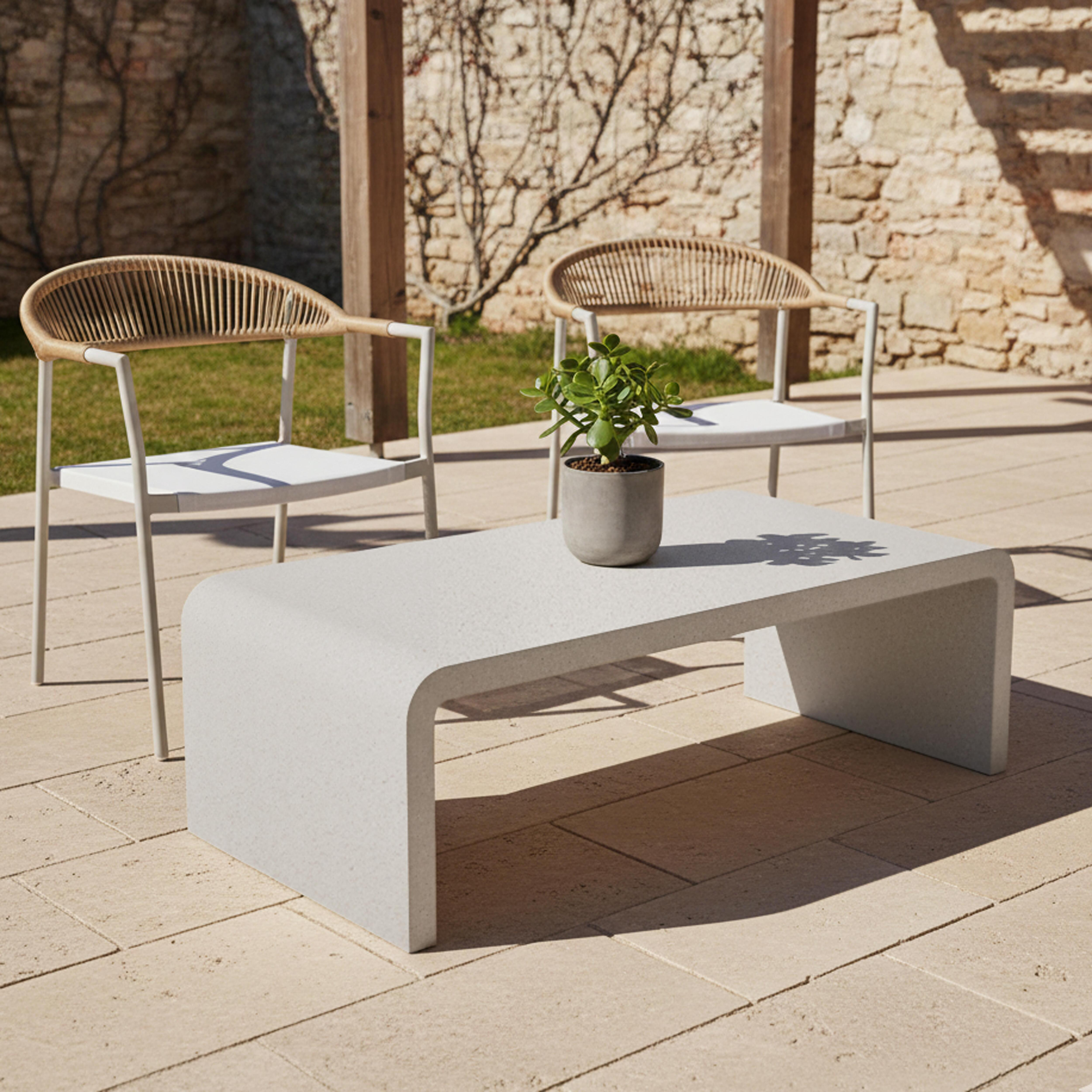 Zwei Stühle und ein Couchtisch mit Pflanze auf einer Terrasse mit Steinboden.
