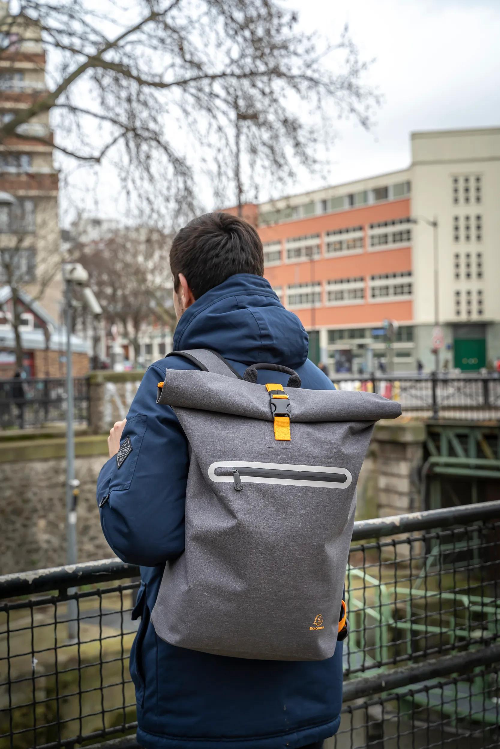 Hombre con chaqueta azul y mochila gris al aire libre.