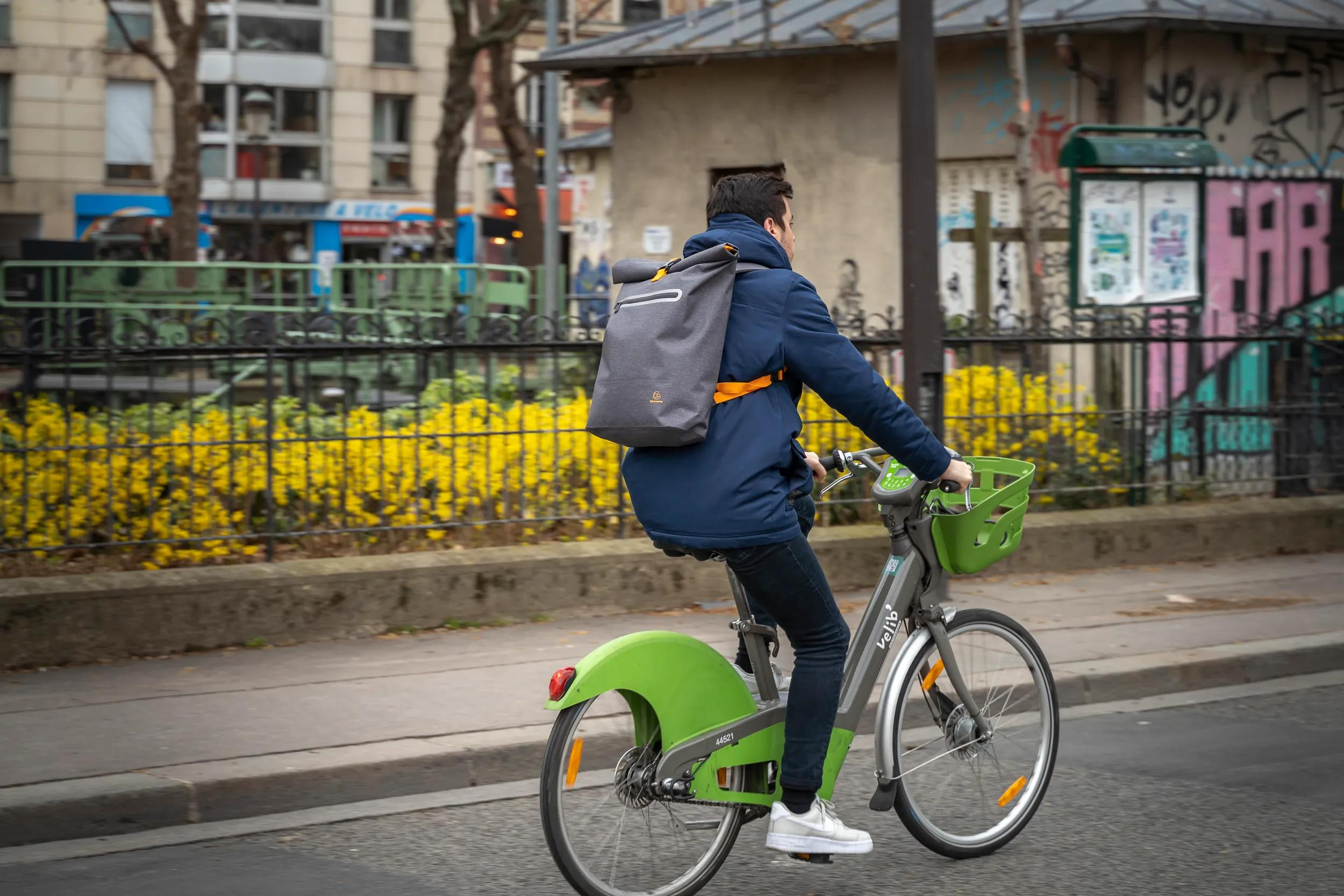 Un hombre monta una bicicleta verde con mochila gris a la espalda en la ciudad.
