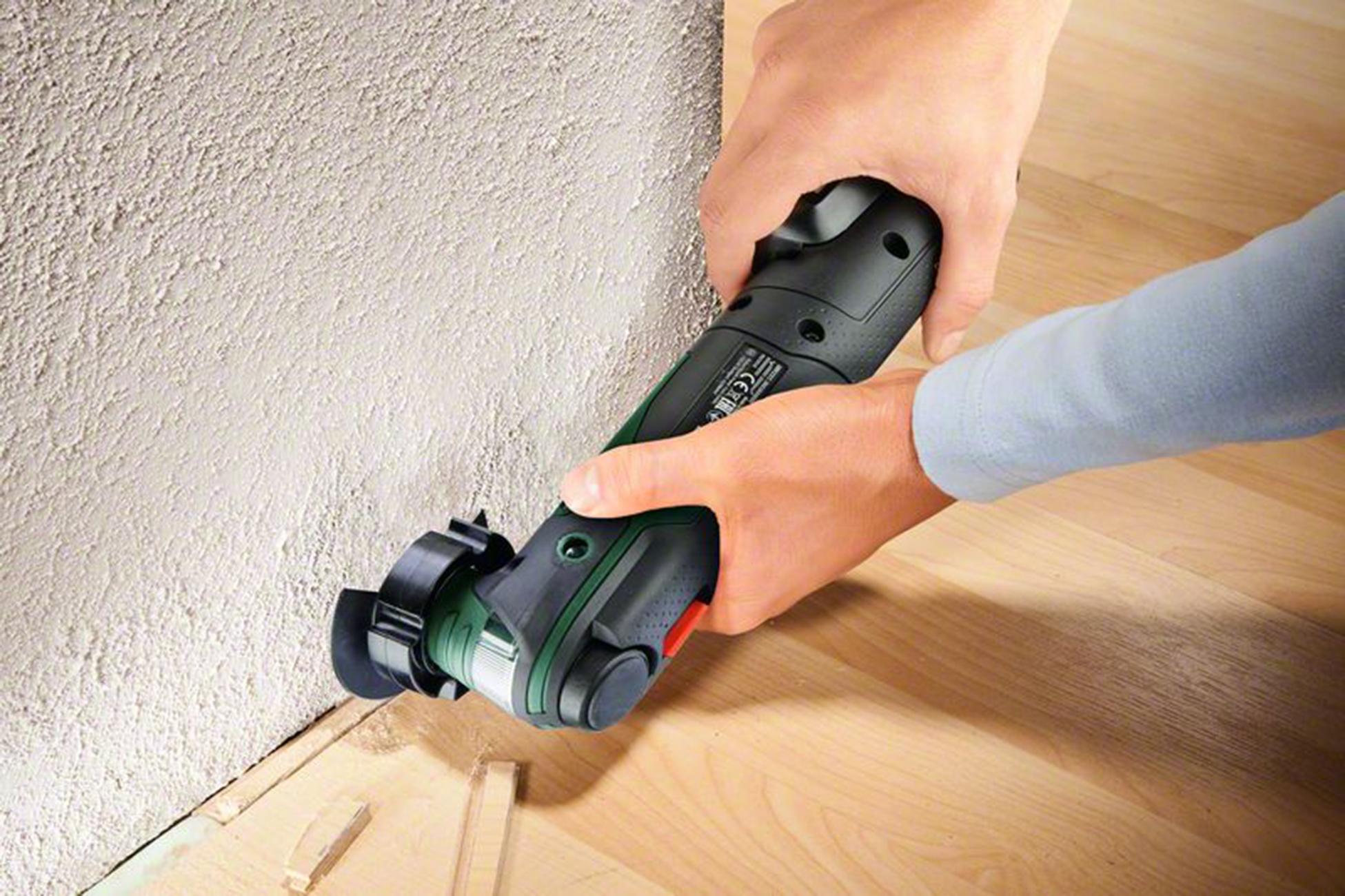 Hände benutzen ein Multifunktionswerkzeug an einer Wand und Holzboden.