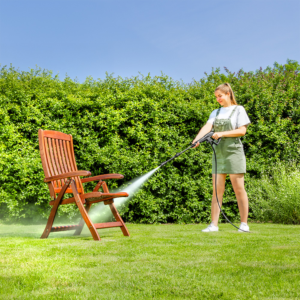 Vrouw reinigt houten stoel met hogedrukreiniger in tuin.