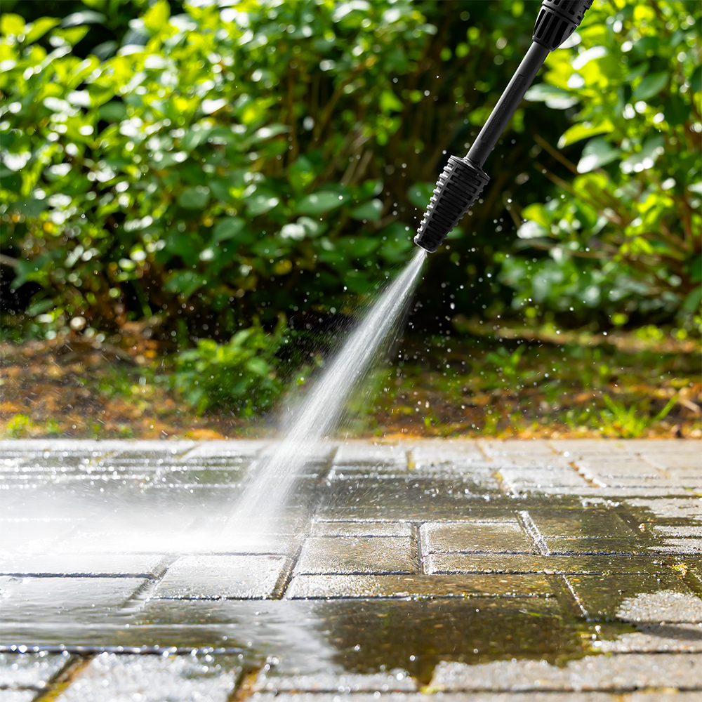 Een hogedrukreiniger sproeit water op een stenen terras om het schoon te maken.
